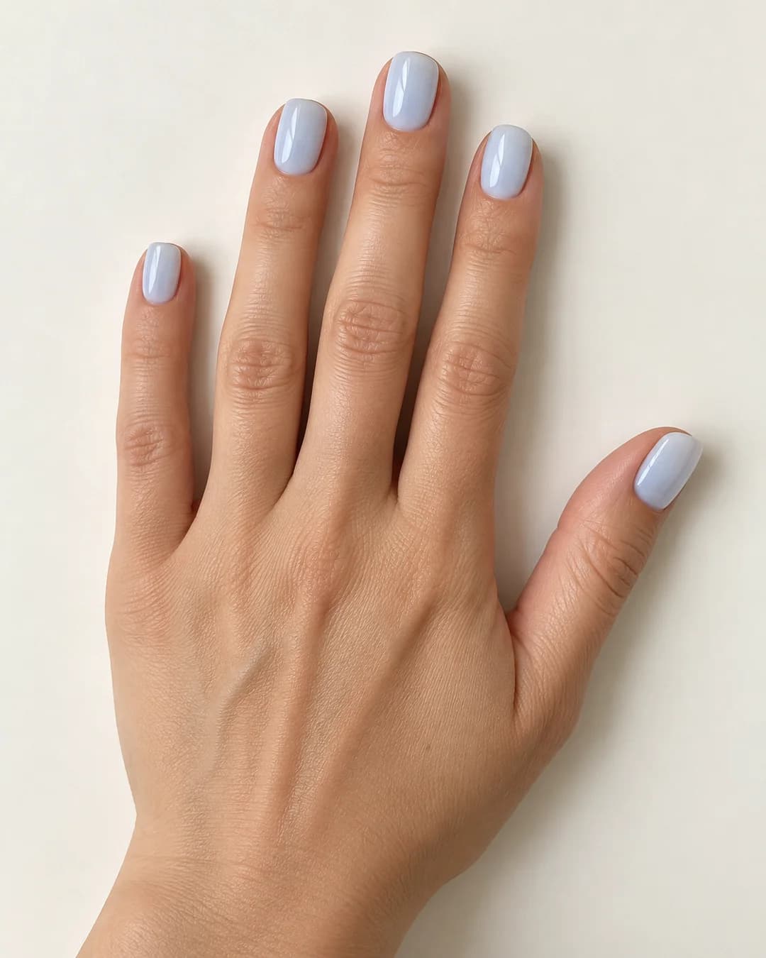 Uñas de forma cuadrada y longitud corta, en azul pastel lechoso de acabado brillante, con esquinas suaves. Detalle de las uñas.