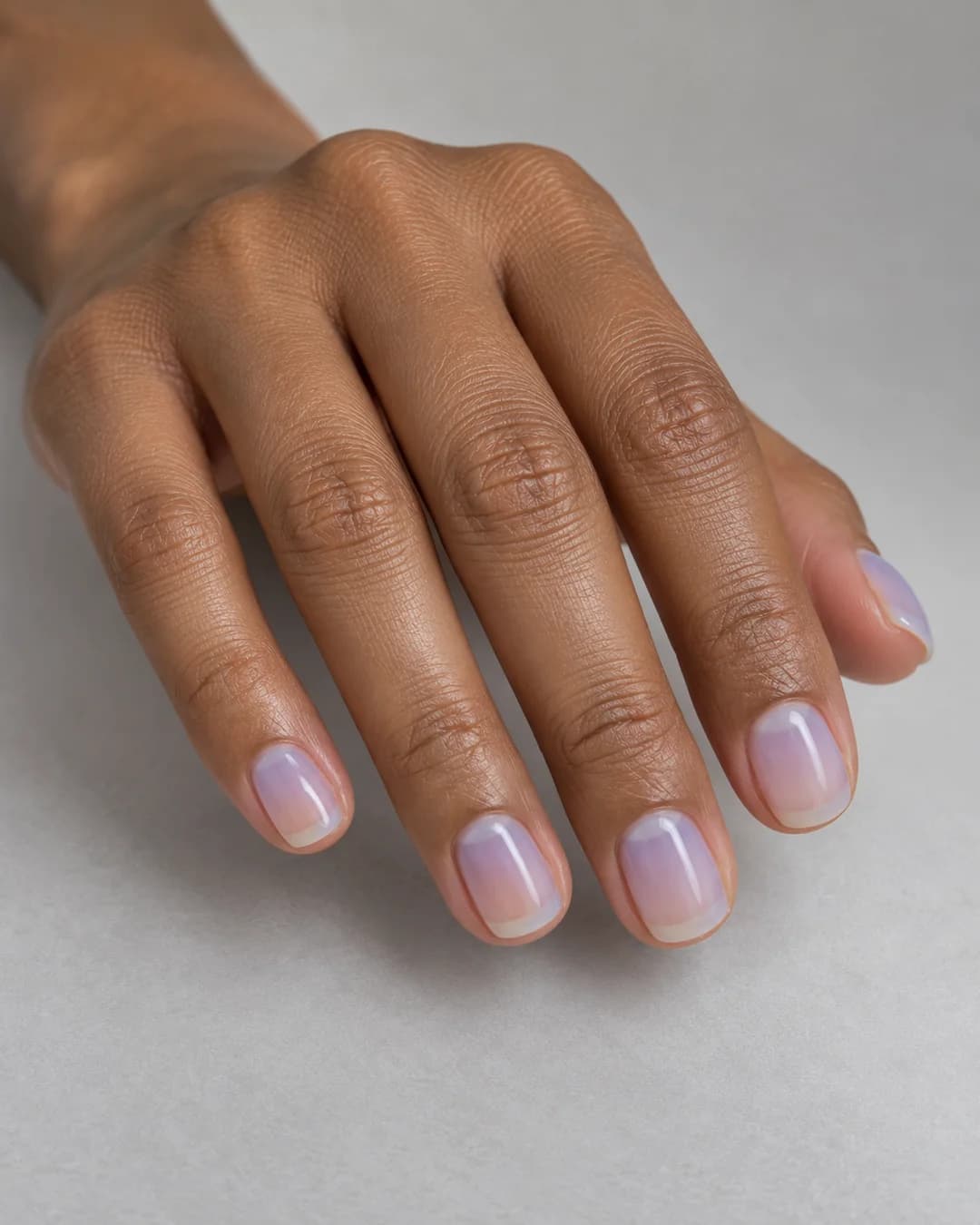 Uñas cortas cuadradas de bordes redondeados de color azul lavanda translúcido y acabado satinado. Vista oblicua de la mano.