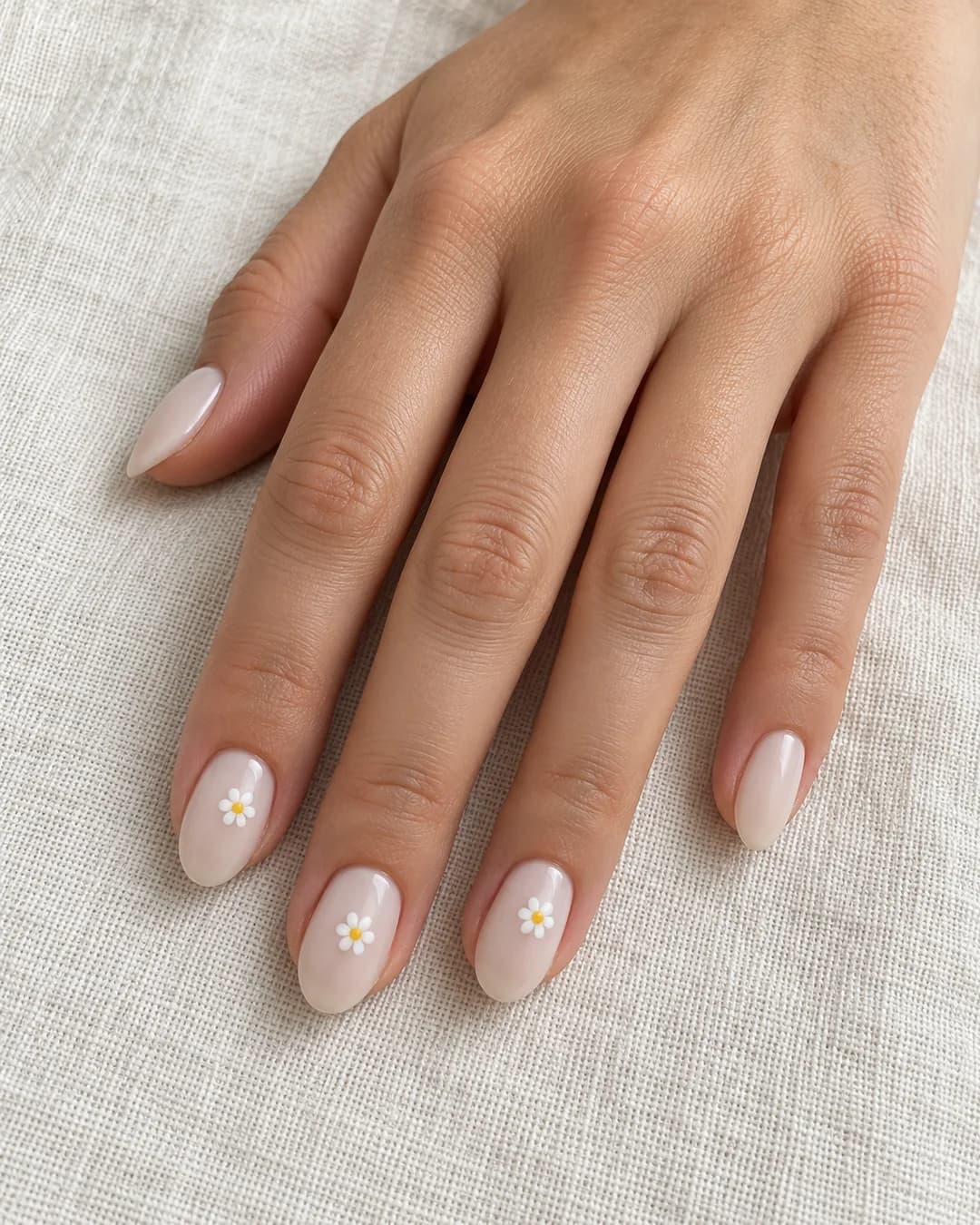 Uñas cortas ovaladas con base blanca lechosa y pequeñas margaritas blancas de centro amarillo. Detalle de las uñas.