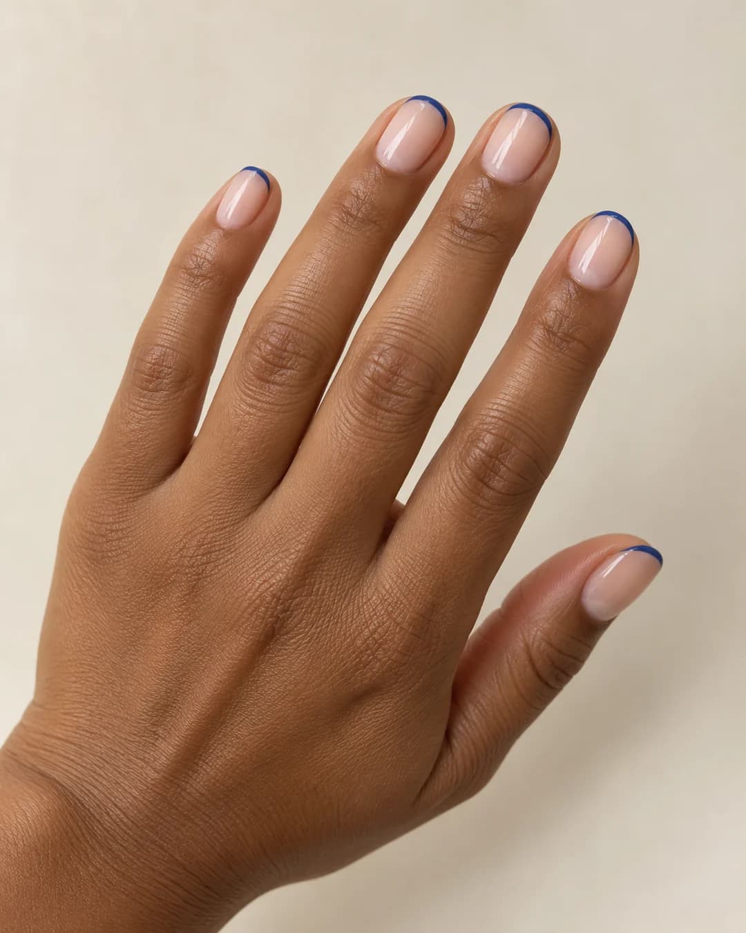 Uñas cortas ovaladas con base nude rosada y una fina punta francesa azul brillante. Vista oblicua de la mano.