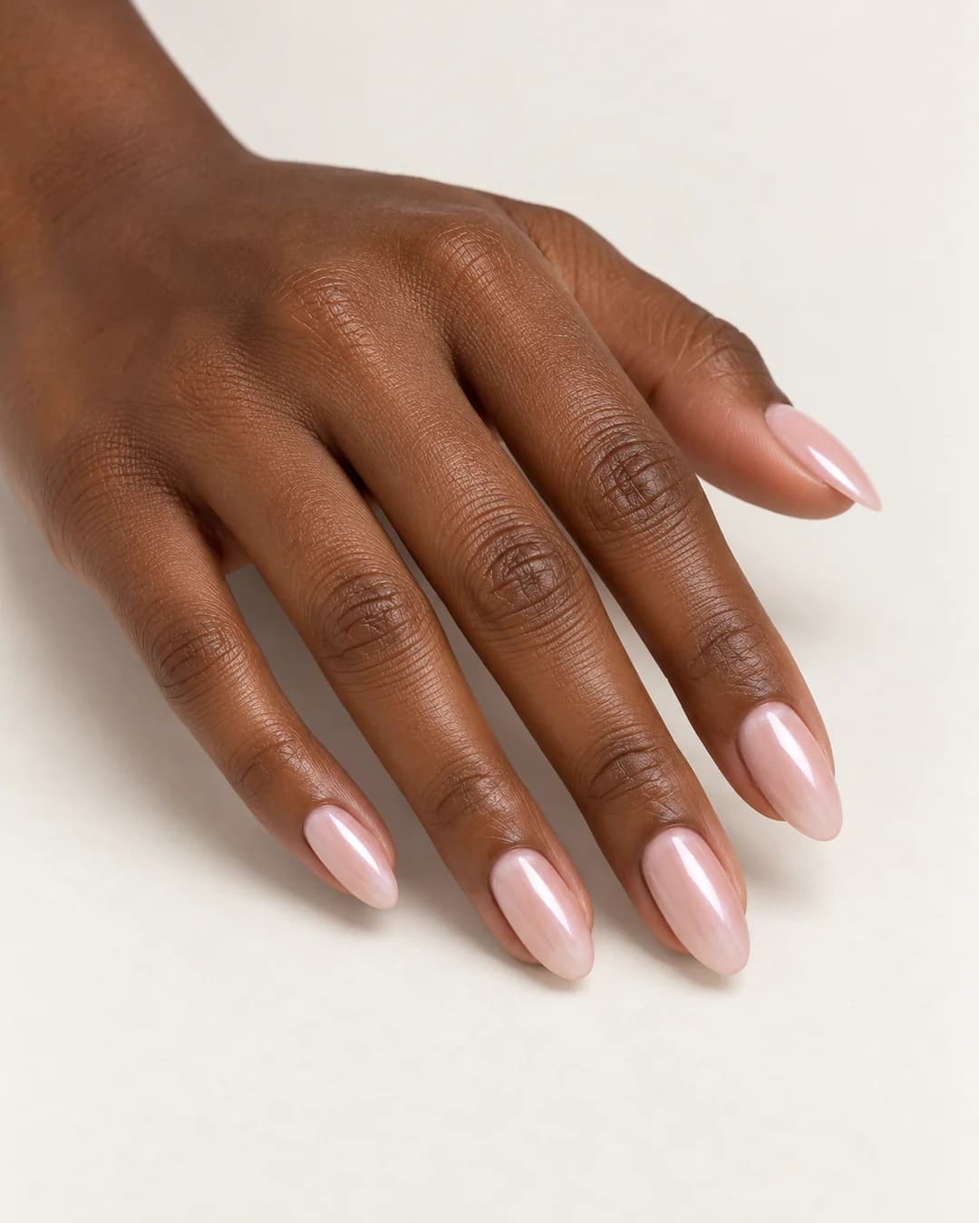 Uñas almendradas de largo medio en nude rosado con reflejo perlado. Vista oblicua de la mano.