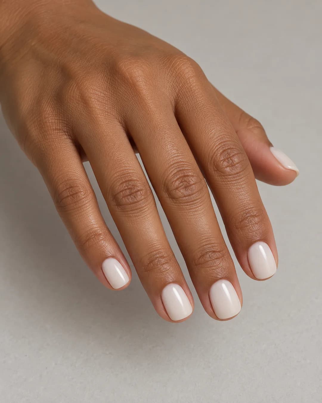 Uñas cortas cuadradas de bordes redondeados de color blanco lechoso uniforme y acabado satinado. Vista oblicua de la mano.