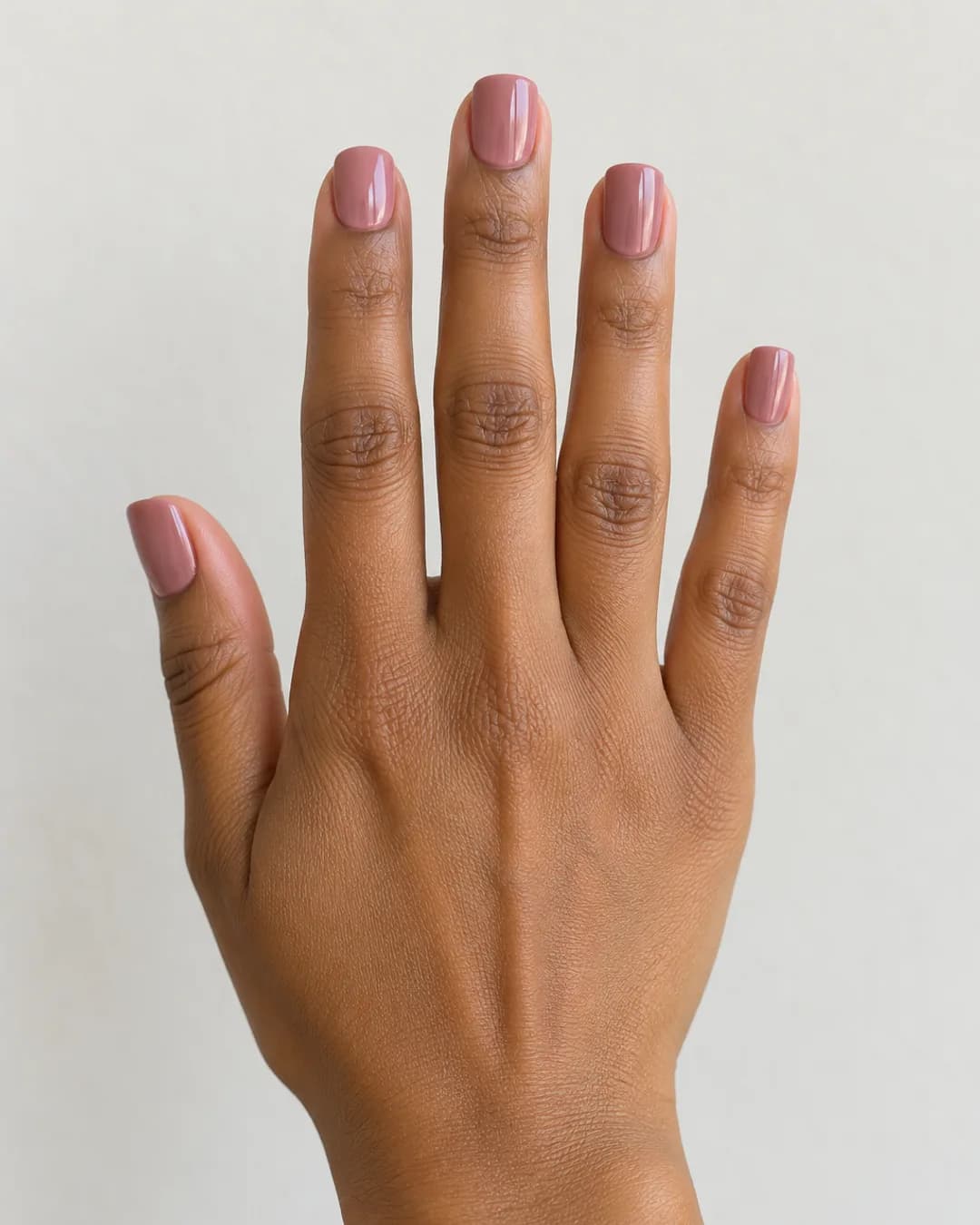 Uñas cortas cuadradas de esquinas suaves en rosa empolvado y acabado brillante. Mano completa.
