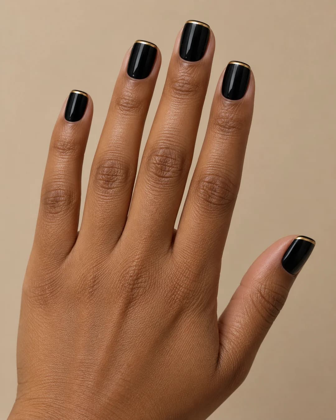 Uñas cortas cuadradas de bordes suaves en negro brillante con una línea dorada en las puntas. Detalle de las uñas.