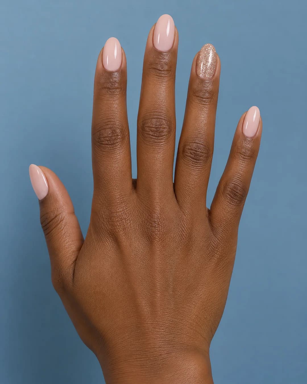 Uñas ovaladas de largo medio en nude rosado con purpurina dorada en el anular. Detalle de las uñas.