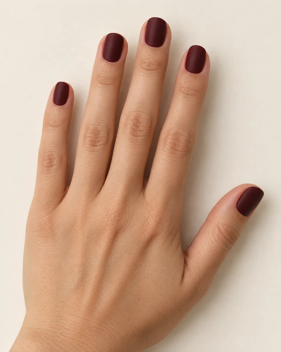 Uñas cortas redondeadas en rojo vino oscuro mate. Detalle de las uñas.