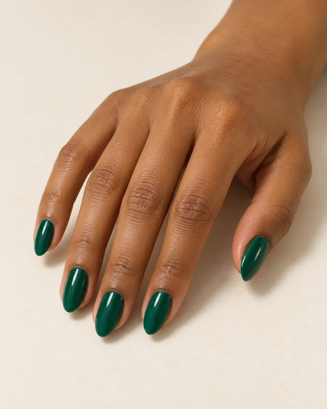 Mano de piel morena con uñas almendradas de largo medio en verde esmeralda brillante. Vista oblicua de la mano.