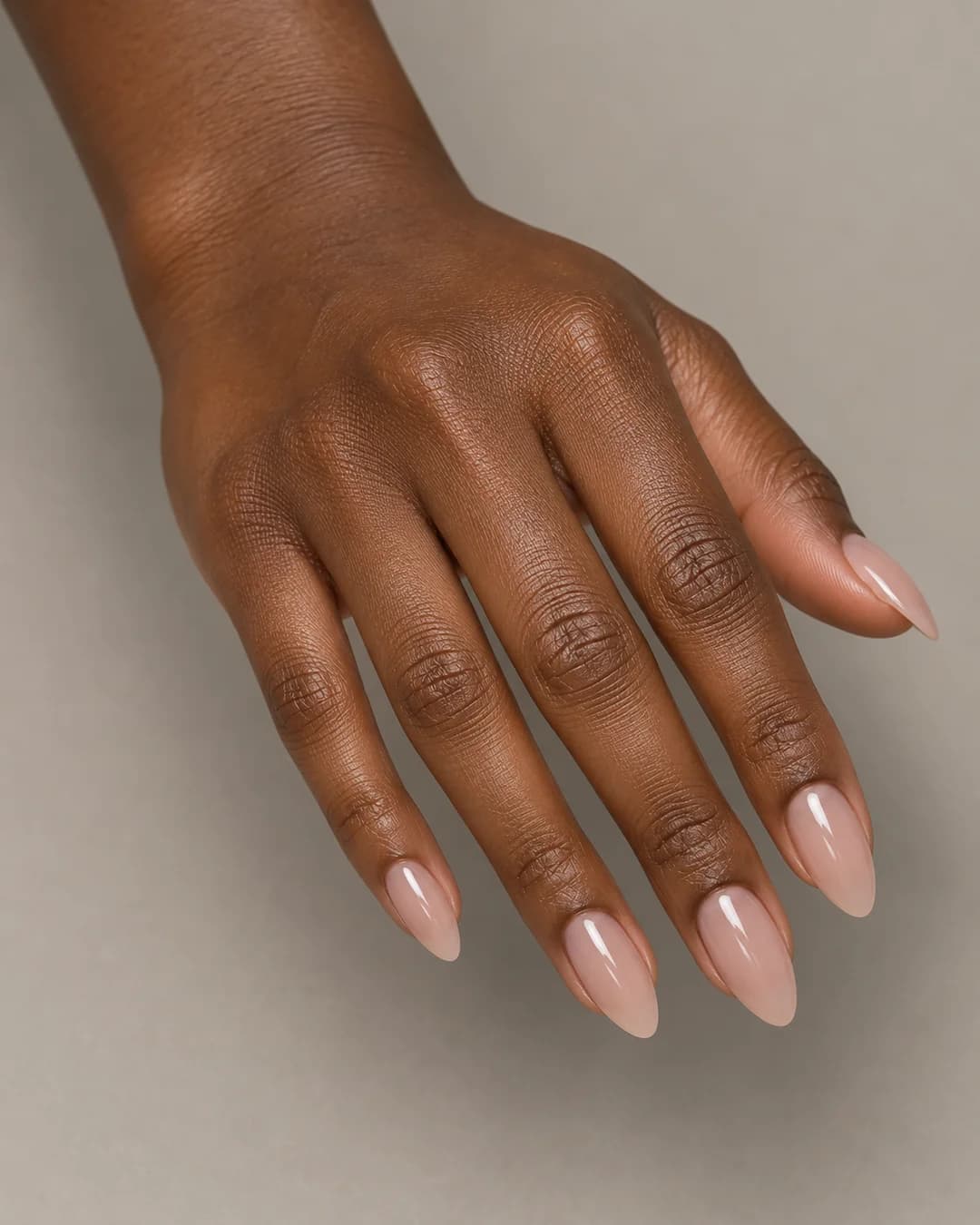 Uñas de forma almendrada y longitud media, en nude rosado translúcido de acabado brillante. Vista oblicua de la mano.