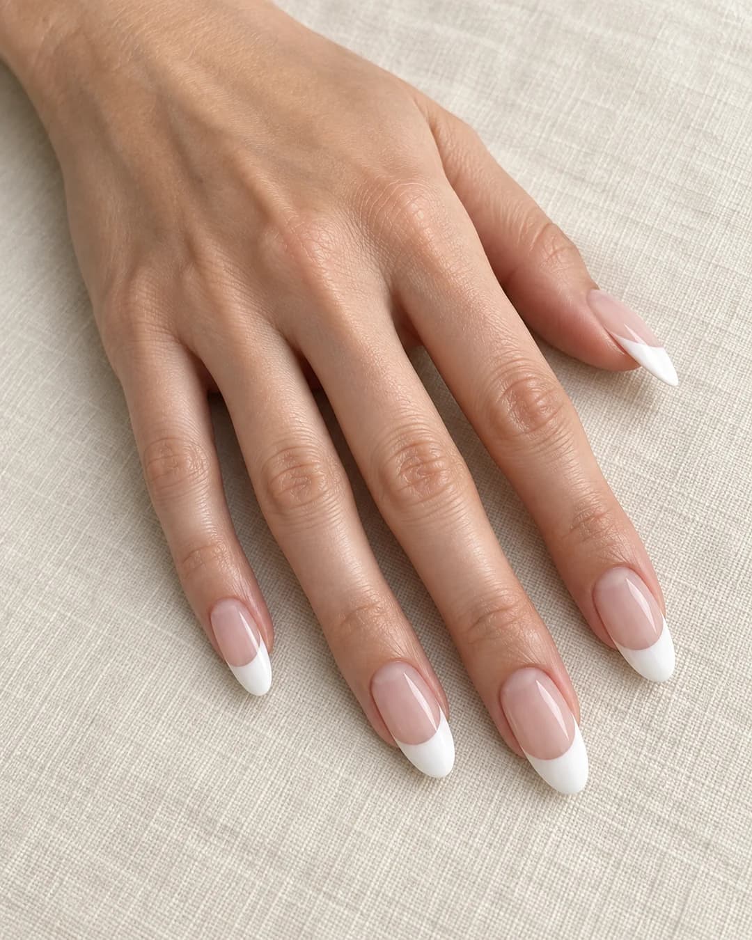 Mano adulta de piel clara con uñas ovaladas largas y manicura francesa de punta blanca ancha.