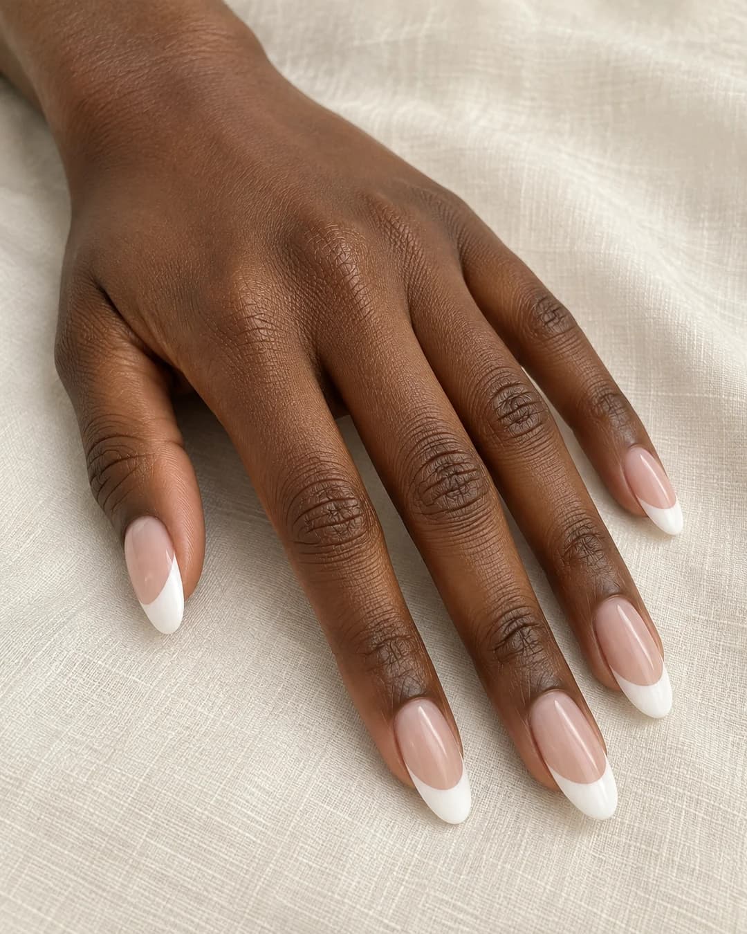 Mano adulta de piel marrón profunda con uñas ovaladas largas y manicura francesa de punta blanca ancha.