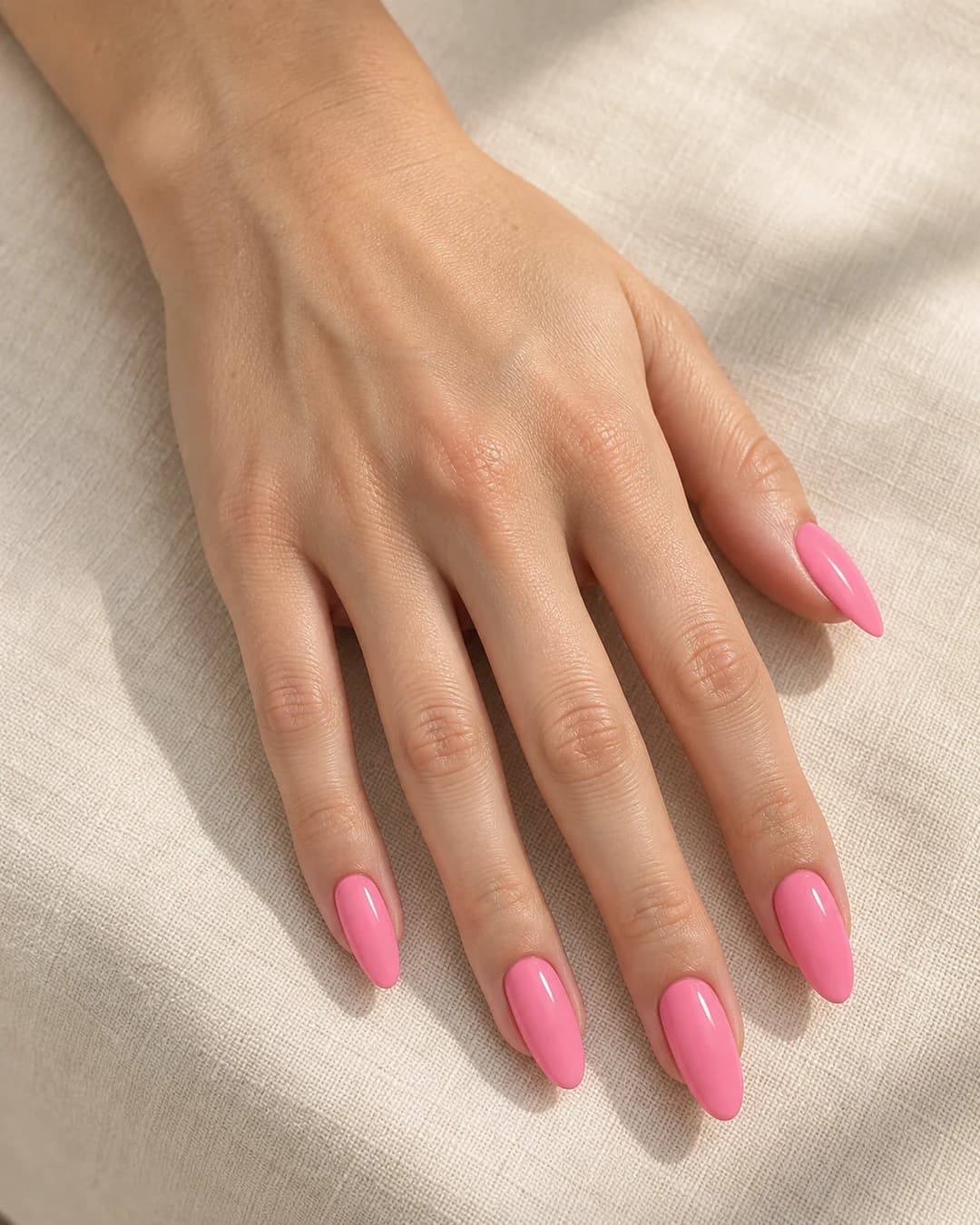 Mano adulta de piel clara con uñas almendradas largas en rosa chicle brillante.