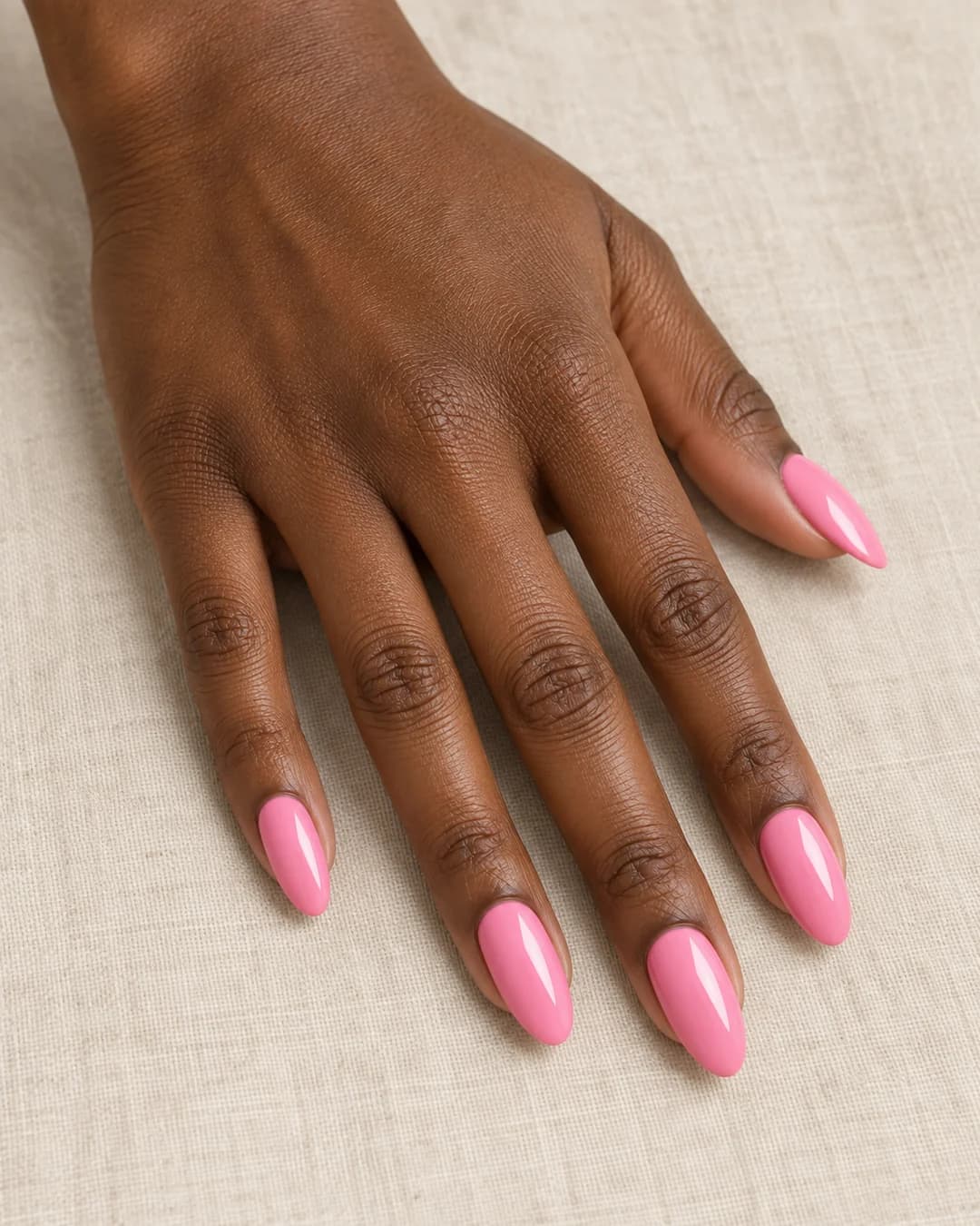 Mano adulta de piel marrón profunda con uñas almendradas largas en rosa chicle brillante.