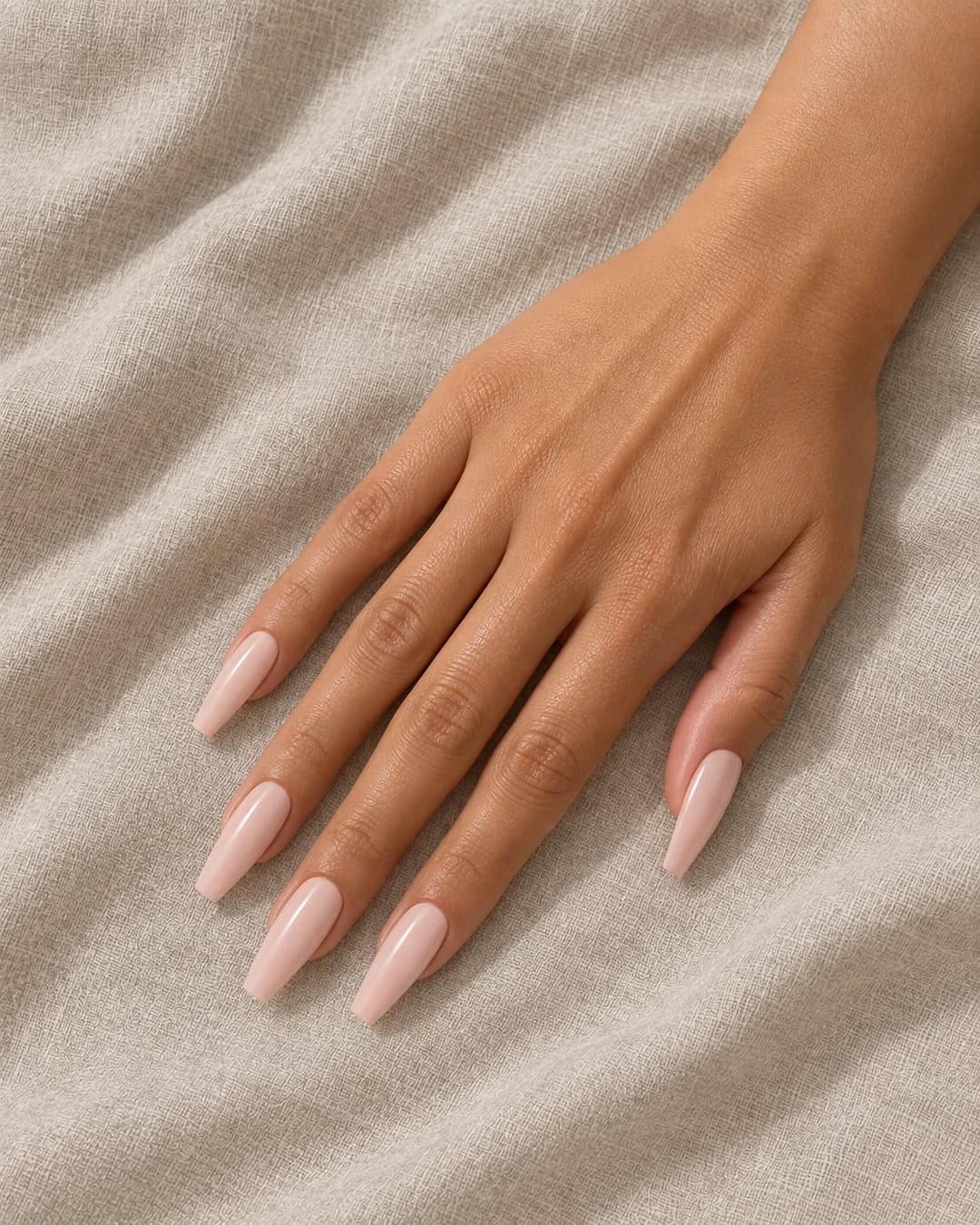 Uñas coffin largas en nude rosa lechoso brillante, cinco puntas completas y enteras sobre piel oliva.
