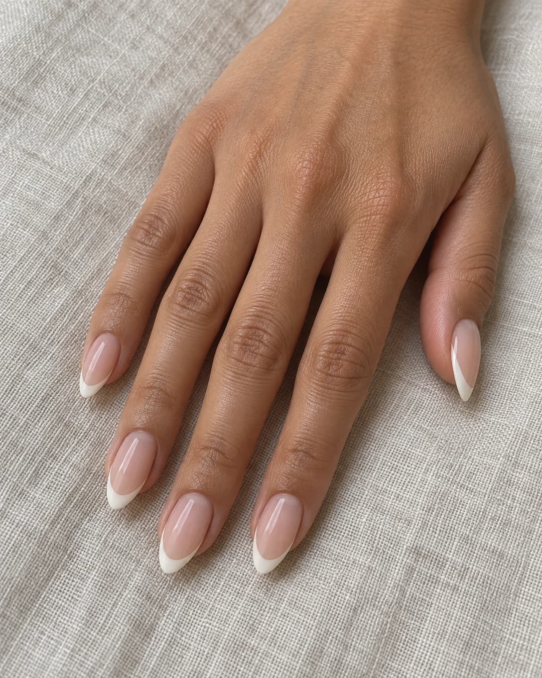 Cinco uñas almendradas de largo medio con base rosa nude y micro-french marfil sobre piel oliva.