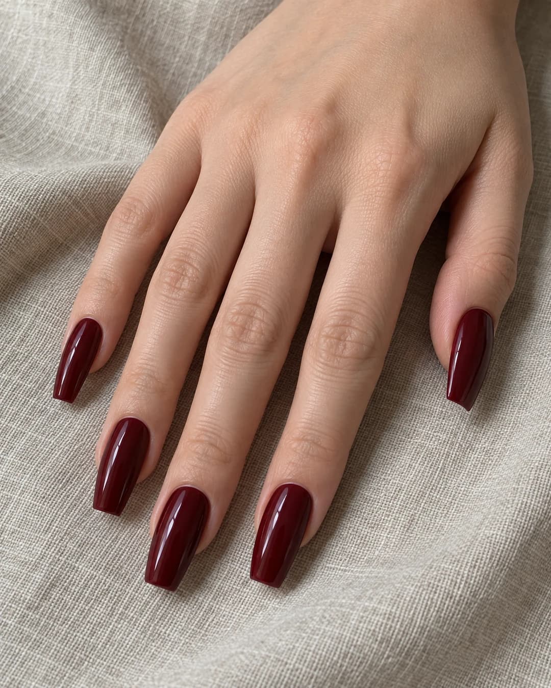 Cinco uñas coffin de largo medio en rojo vino brillante sobre piel clara.