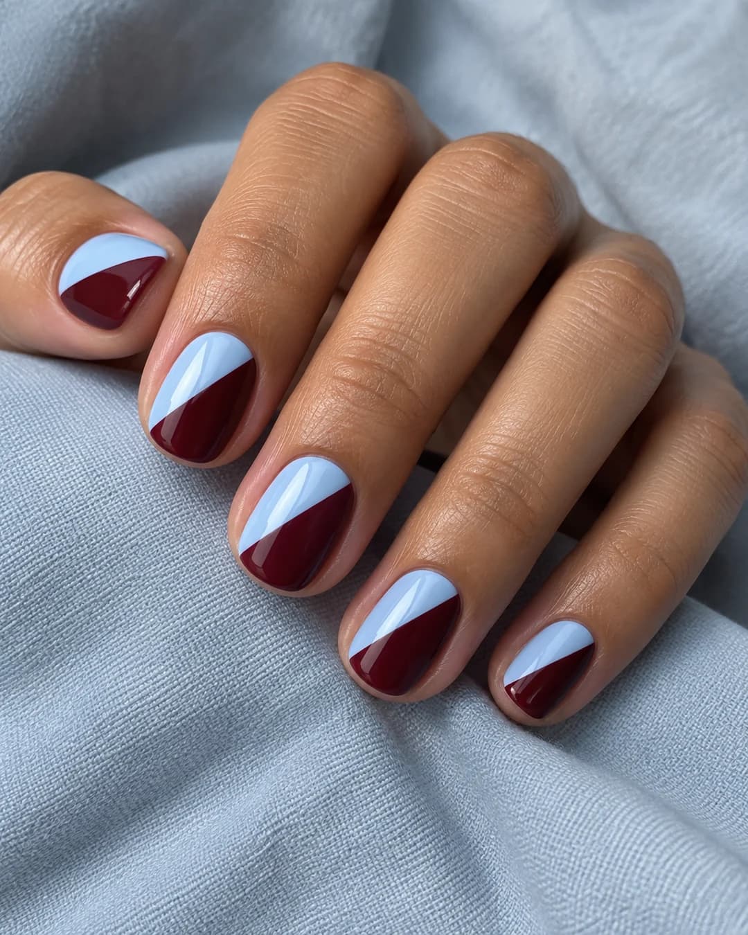 Mano de piel marrón oscura con uñas almendradas medianas en burdeos con puntas francesas azul bebé.