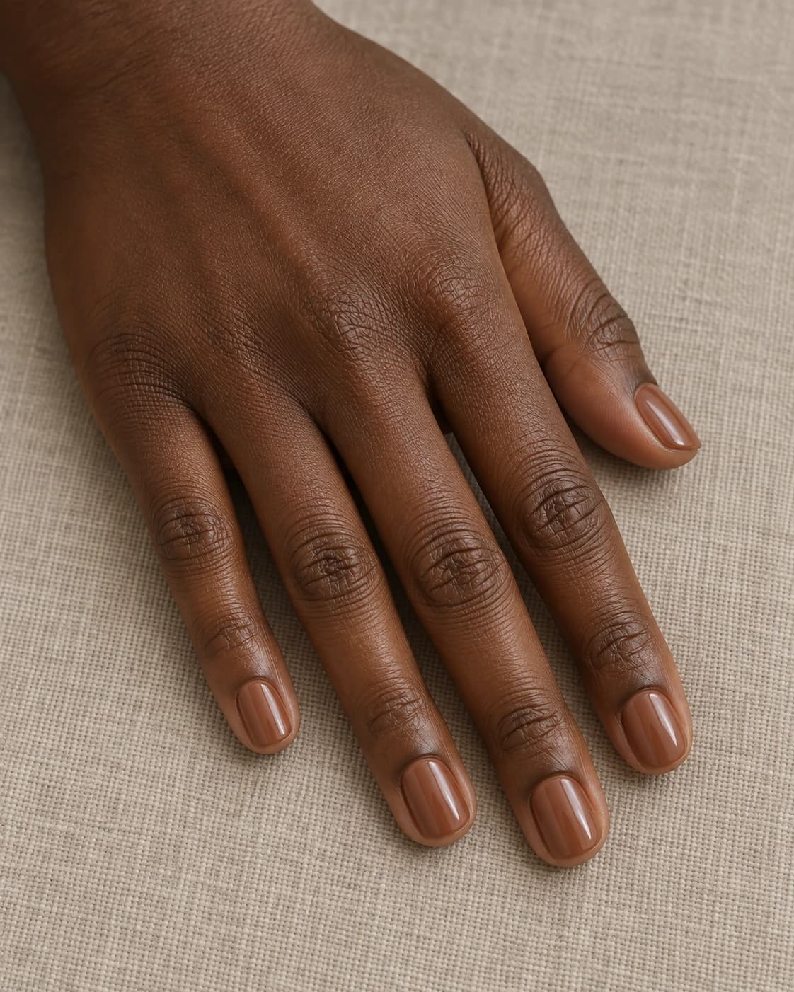Uñas cortas squoval en caramelo suave translúcido sobre una mano adulta de piel marrón profunda.