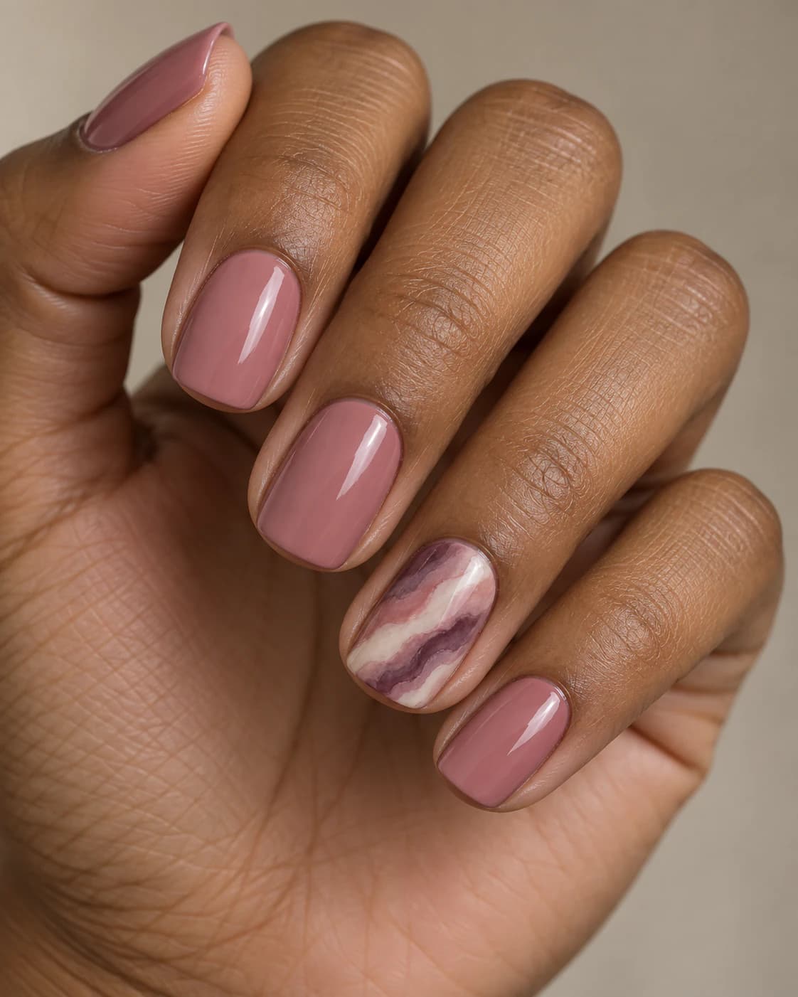 Uñas cortas squoval en rosa empolvado; el anular tiene bandas acuarela diagonales en malva, ciruela y marfil.