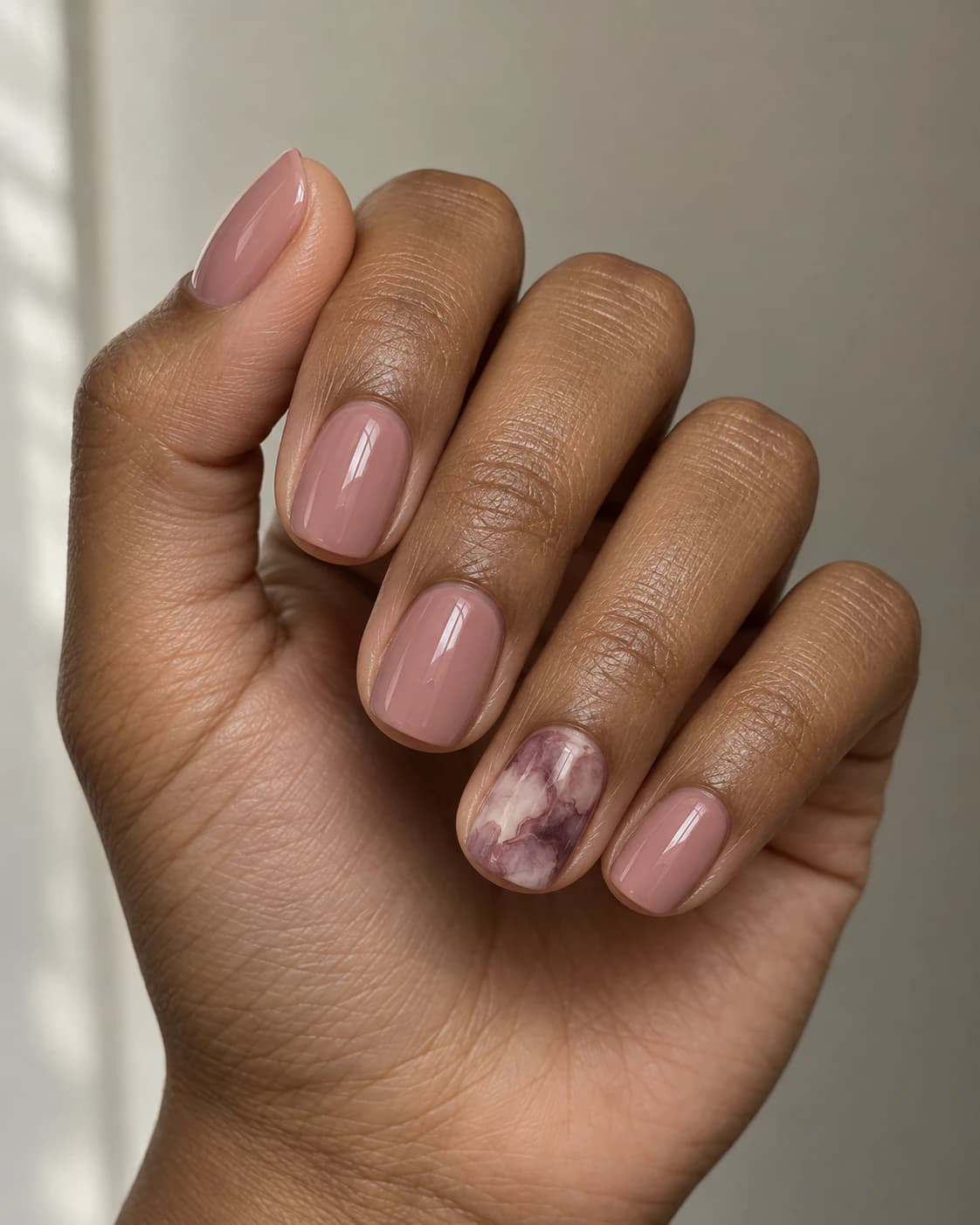 Uñas cortas squoval en rosa empolvado; el anular presenta nubes marmoleadas de malva, ciruela y marfil.
