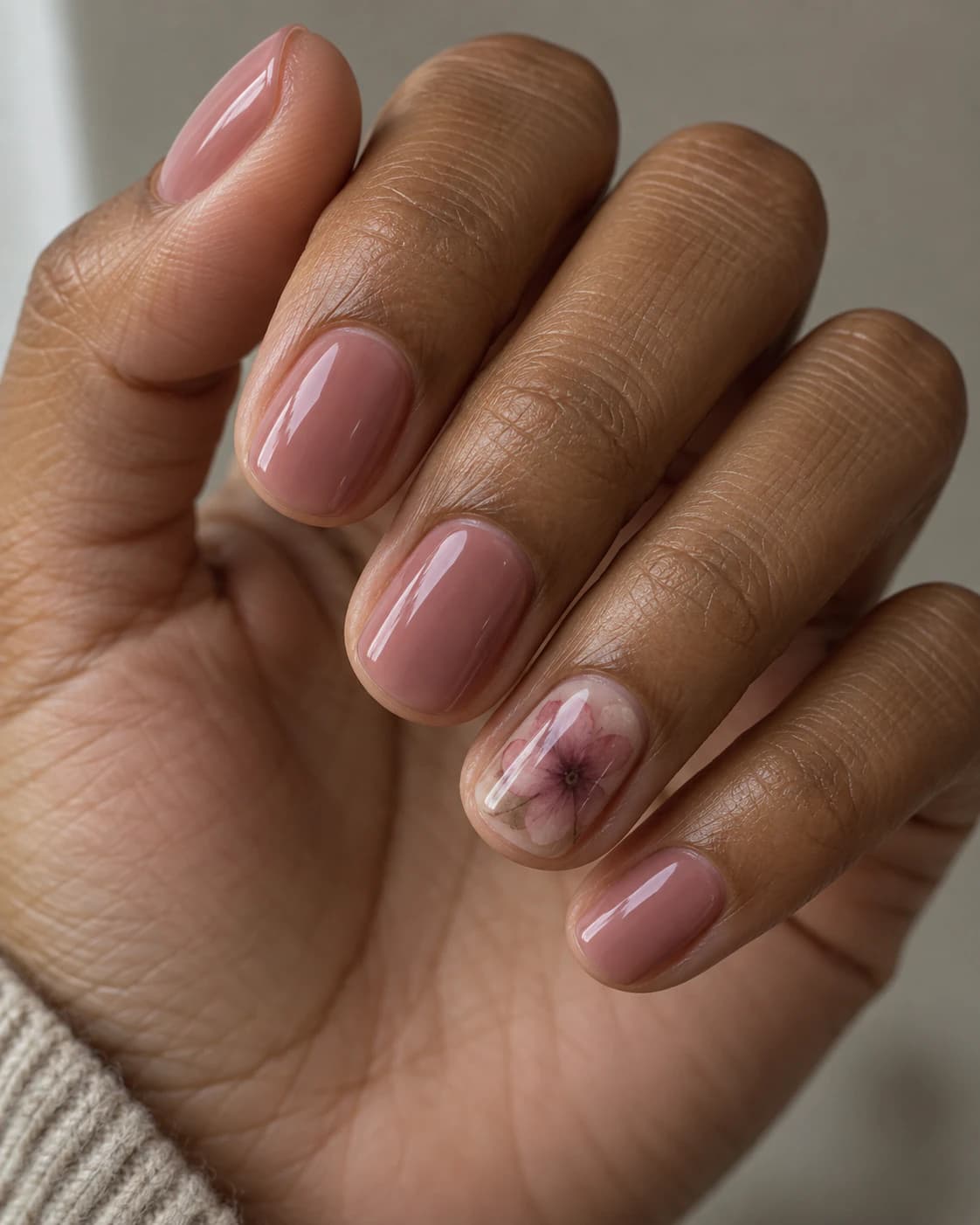 Uñas cortas squoval en rosa empolvado; el anular muestra pétalos difusos en tonos malva y ciruela.