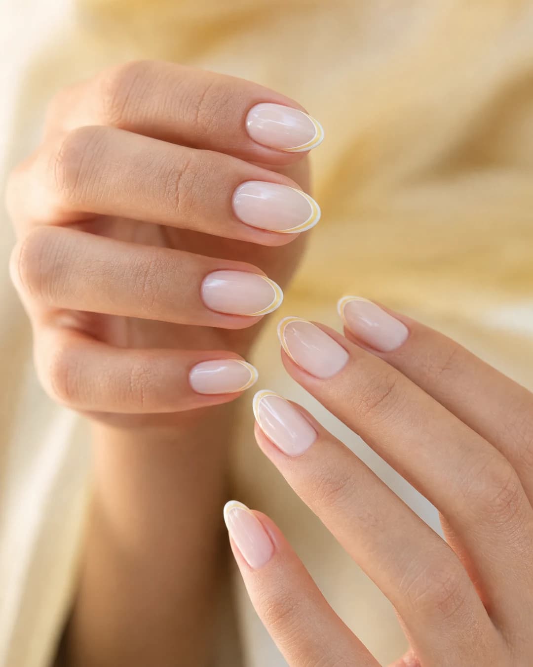 Uñas almendradas con doble línea ultrafina en amarillo mantequilla y blanco roto sobre base lechosa