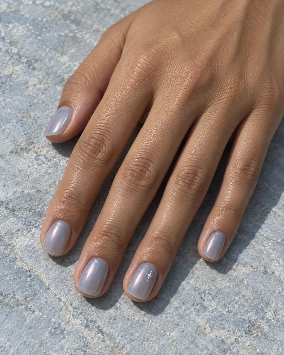 Mano adulta de piel oliva con uñas cortas squoval en azul bruma translúcido y una microestrella plateada de cuatro puntas en el anular.