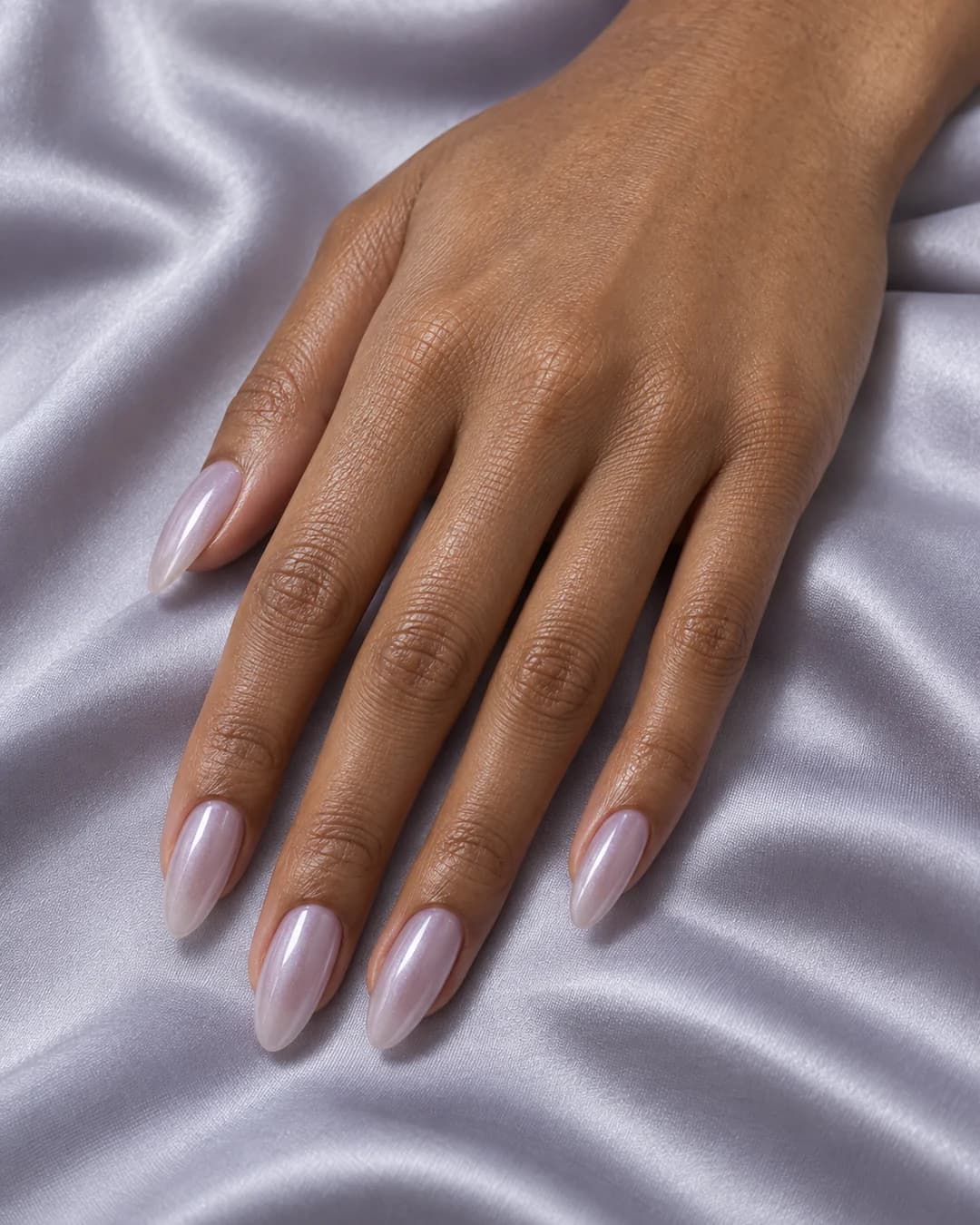 Mano adulta de piel canela media con uñas almendradas medias en lavanda pálida translúcida y brillo perlado suave.