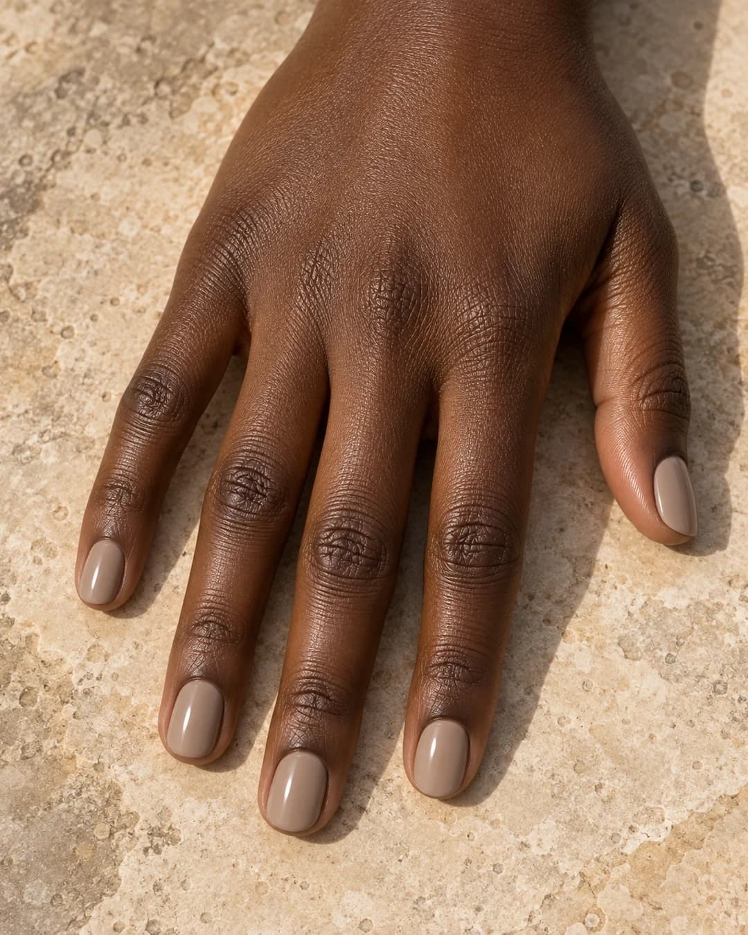 Uñas chai latte cortas y redondeadas en taupe cálido sobre piel profunda.
