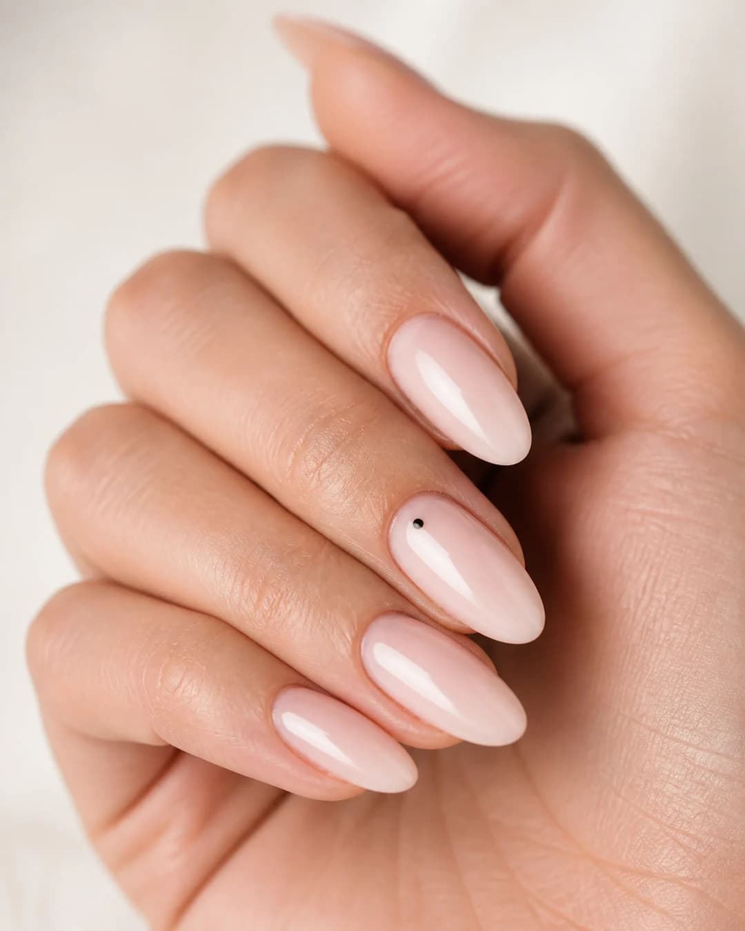 Uñas nude con un punto único negro cerca de la cutícula del anular