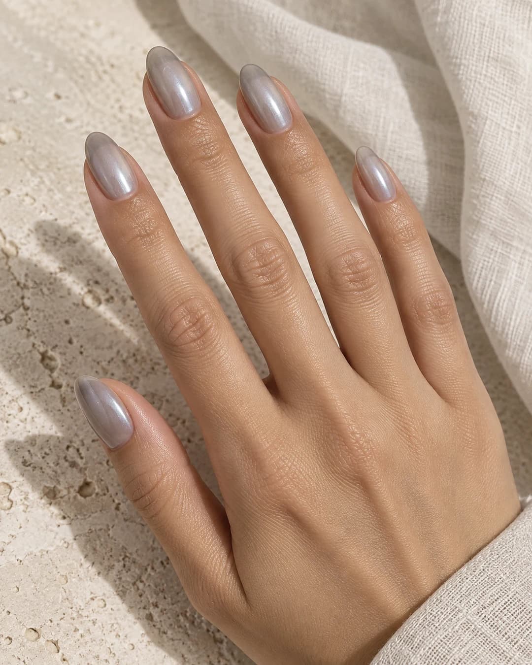 Uñas gris perla translúcidas en almendra media con reflejo plateado suave sobre piel media