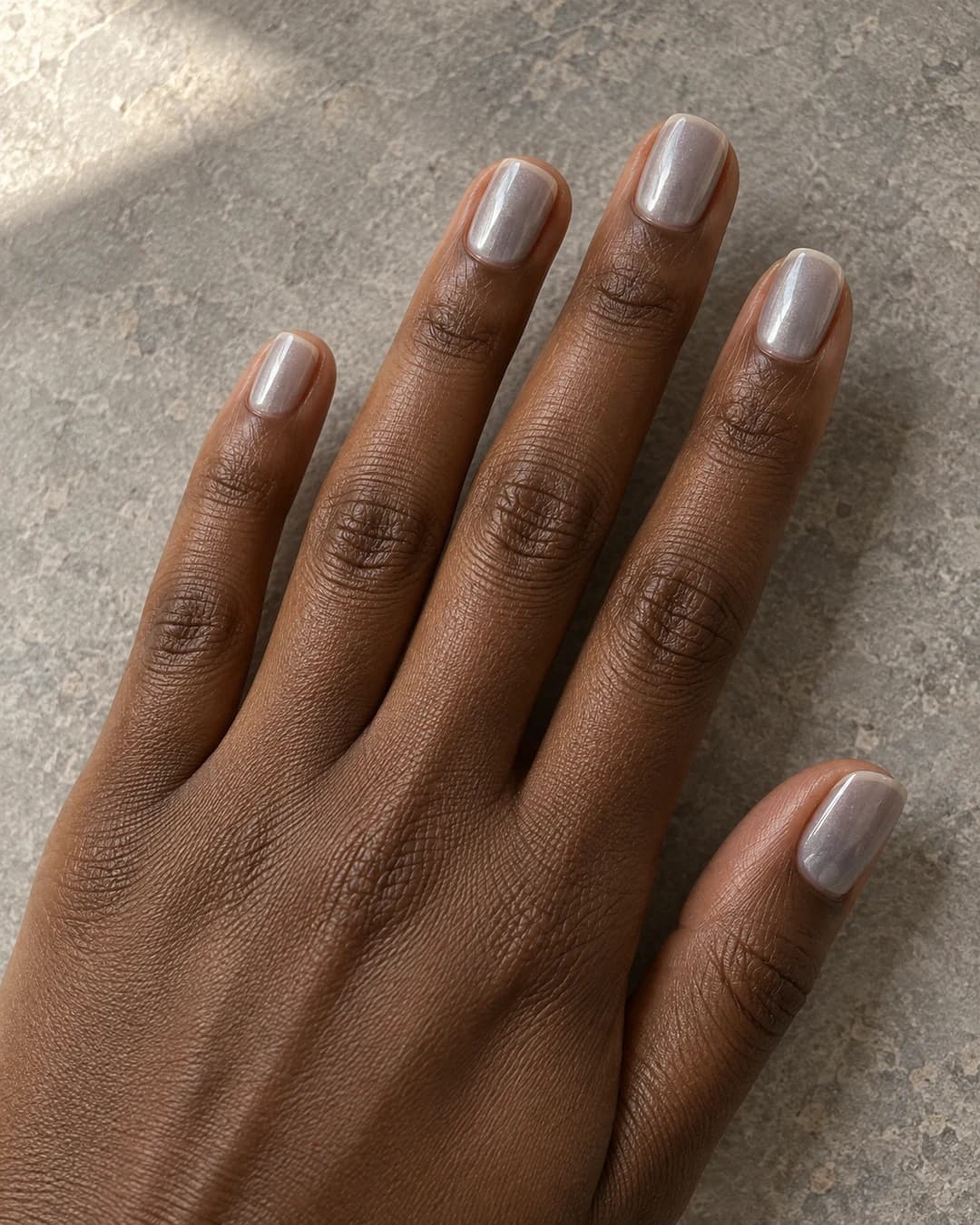 Uñas gris perla translúcidas en forma squoval corta, con reflejo suave sobre piel morena