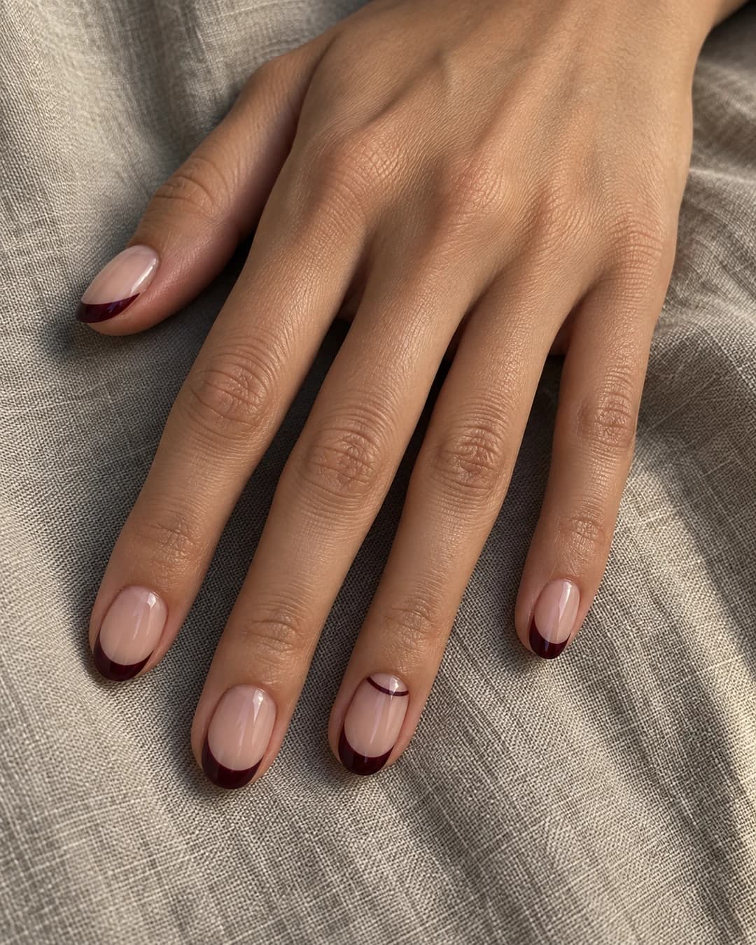 Mano de piel oliva con uñas ovaladas rosa translúcido y puntas francesas burdeos
