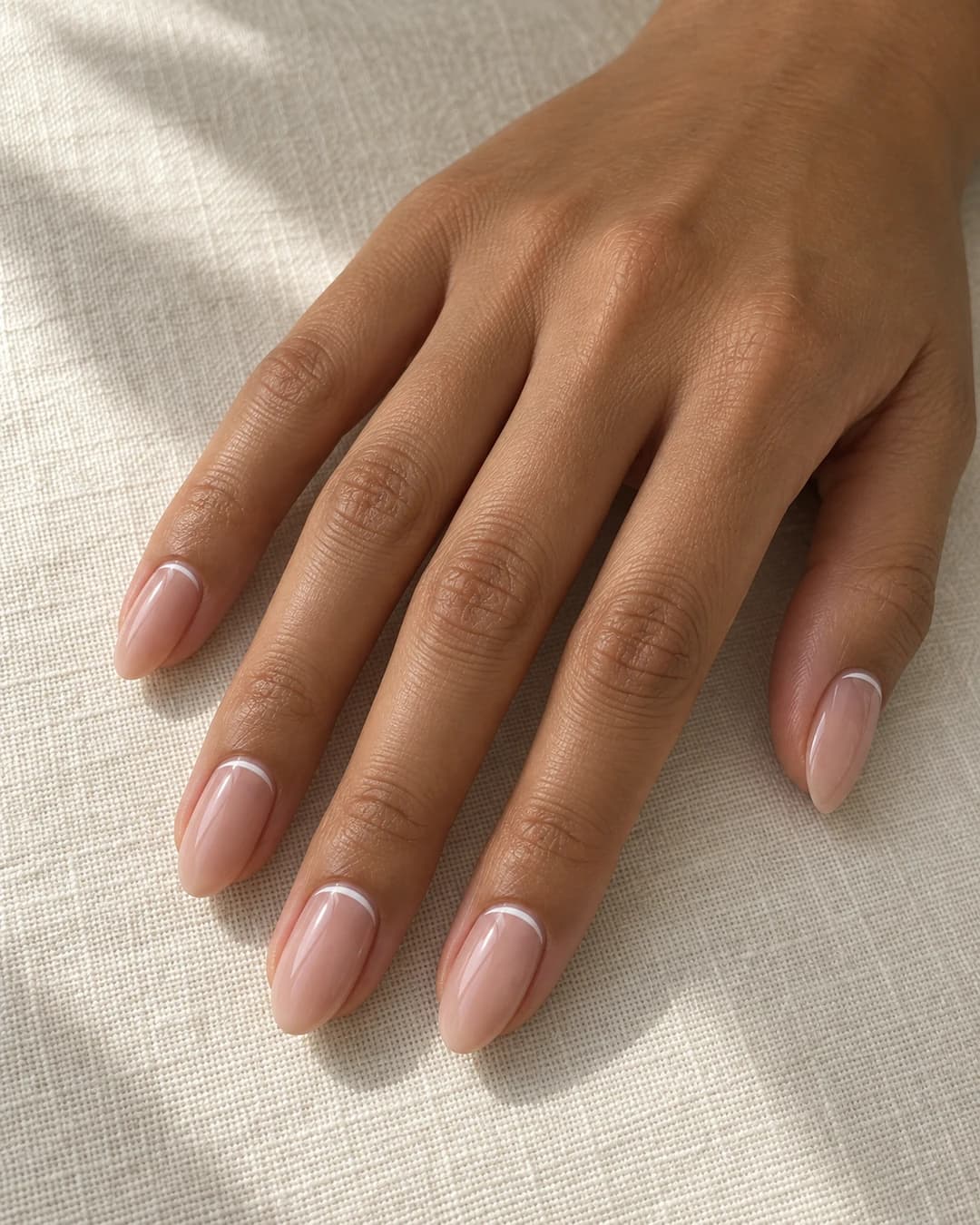 Uñas almendradas medias con arco francés blanco fino junto a la cutícula y borde libre nude.