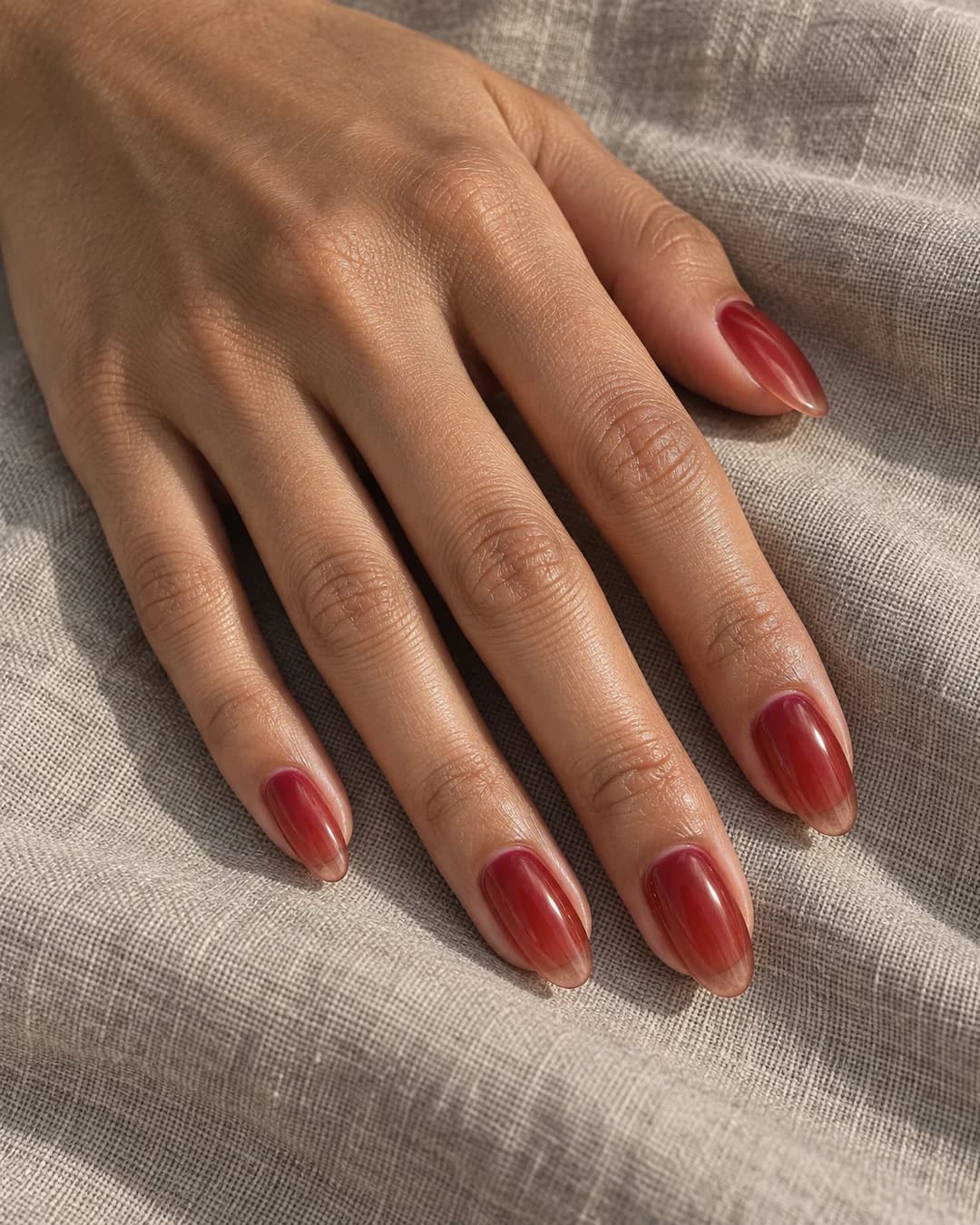 Uñas almendradas medias en rojo cereza tipo gelatina, translúcido y brillante, sobre una mano adulta de piel oliva.