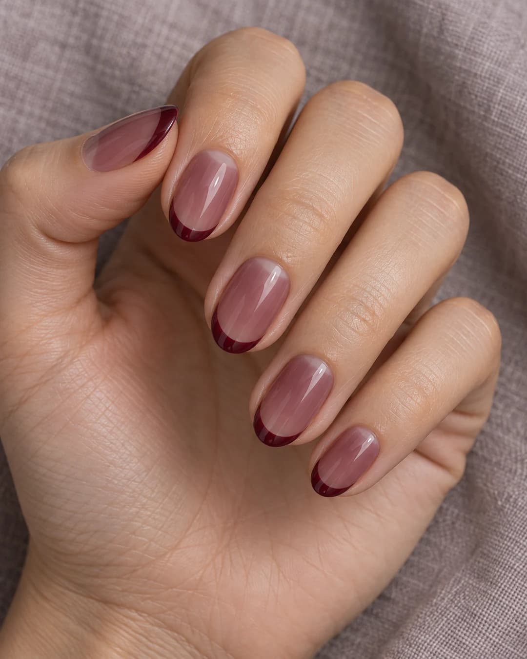 Mano con uñas almendradas de base jelly berenjena translúcida y puntas francesas granate intenso.