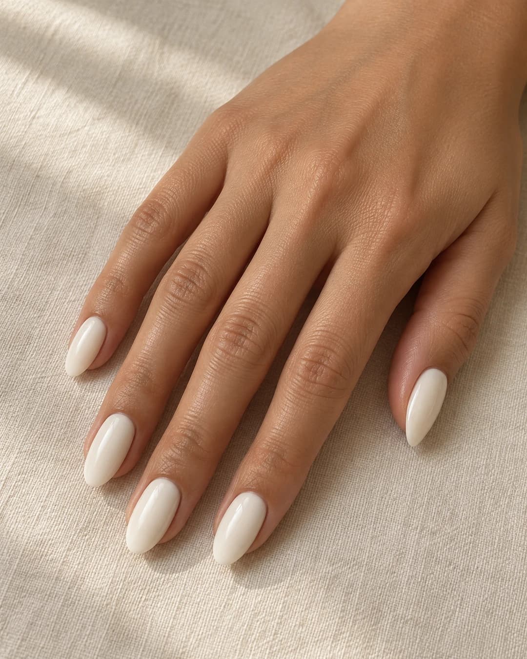 Uñas almendradas medias con base crema lechosa opaca y cobertura uniforme de tono marfil cálido.