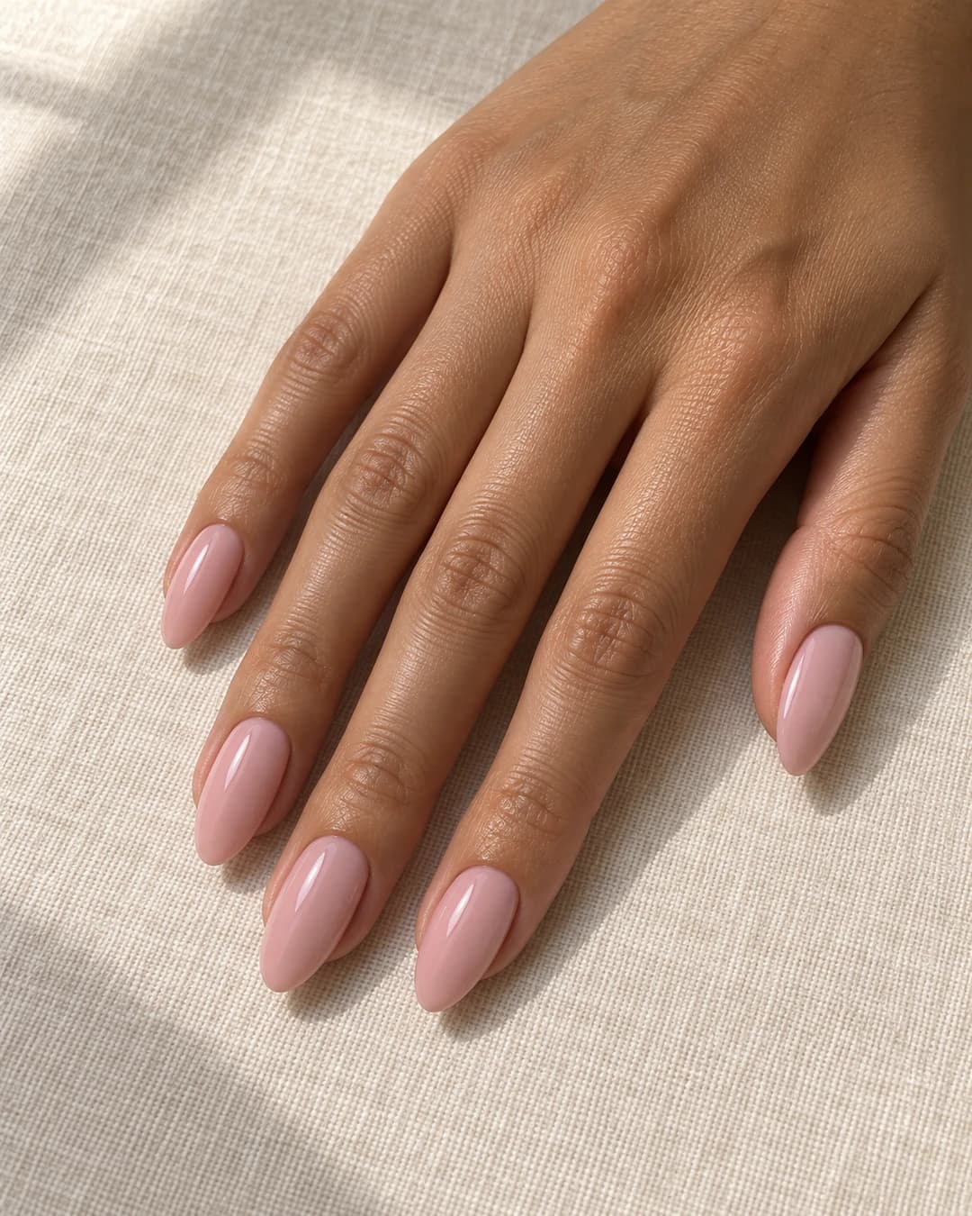 Uñas almendradas medias con base rosa lechosa opaca y cobertura uniforme sin línea natural visible.