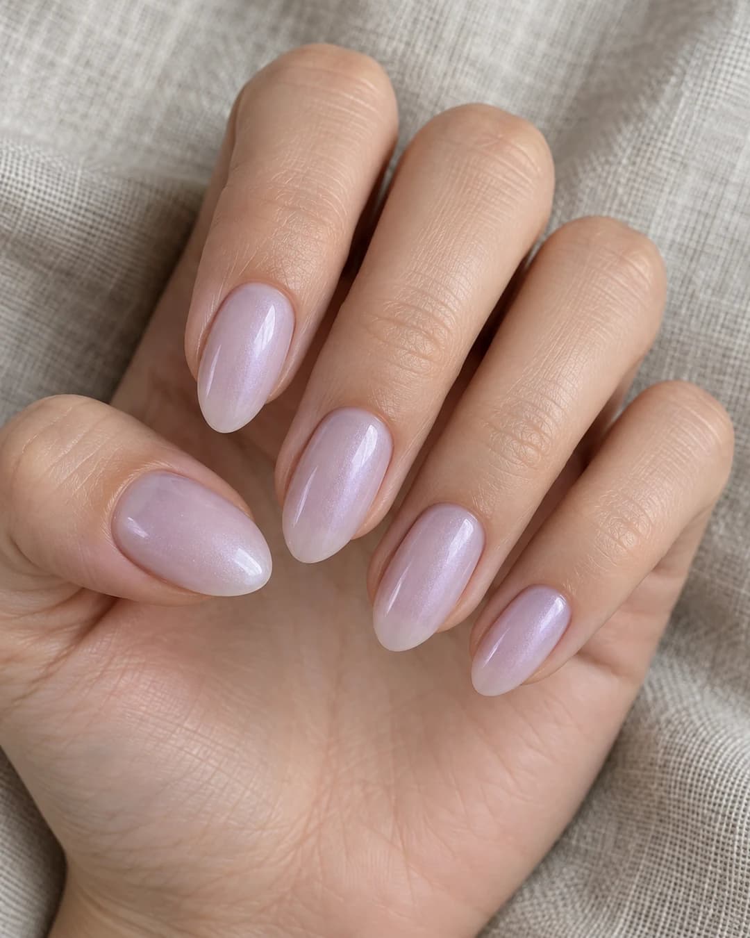 Mano adulta de piel clara con uñas almendradas medias en lavanda lechoso y reflejo perlado sutil.