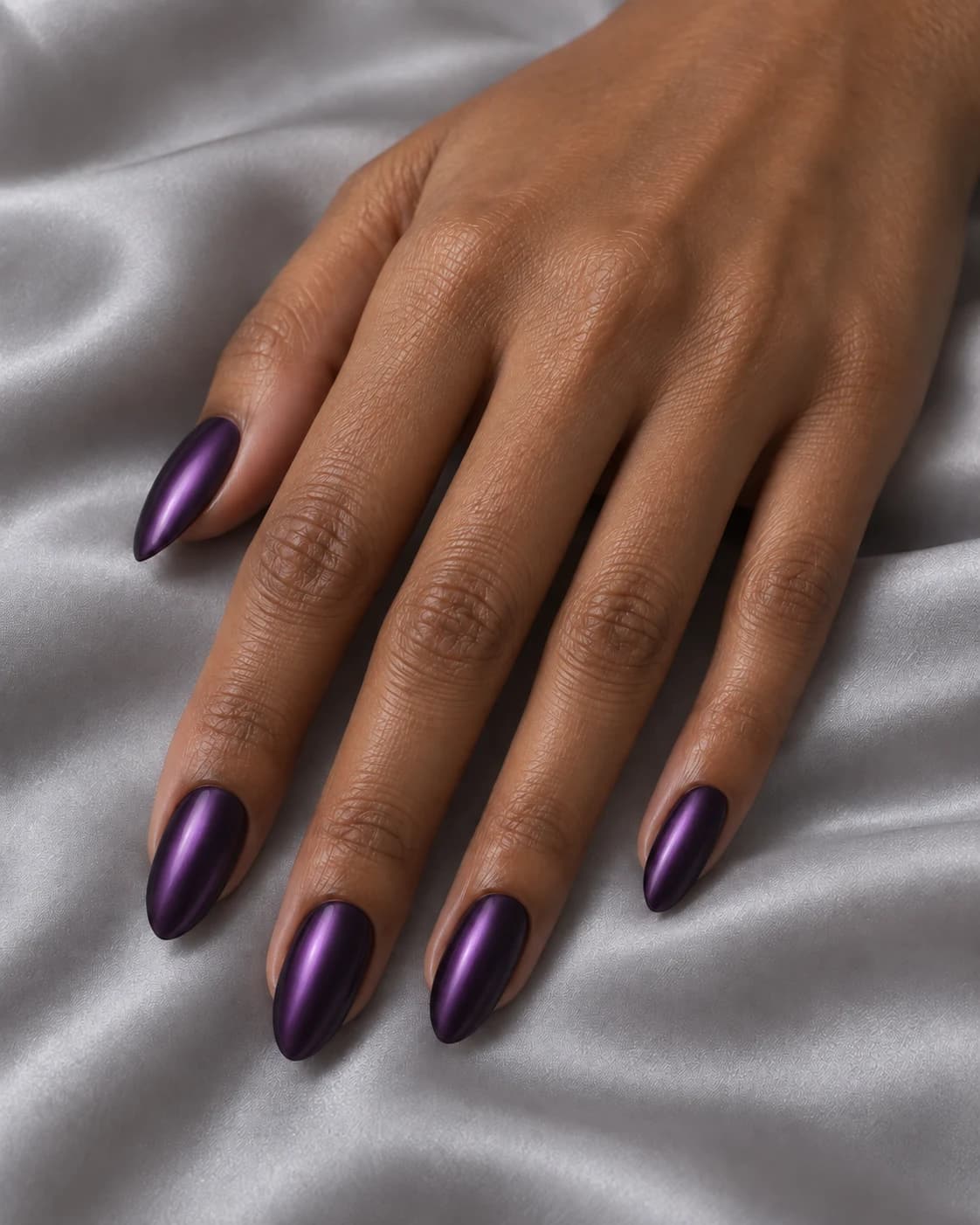 Mano adulta de piel oliva con cinco uñas almendradas medias en morado noche y reflejo violeta cromado difuso.