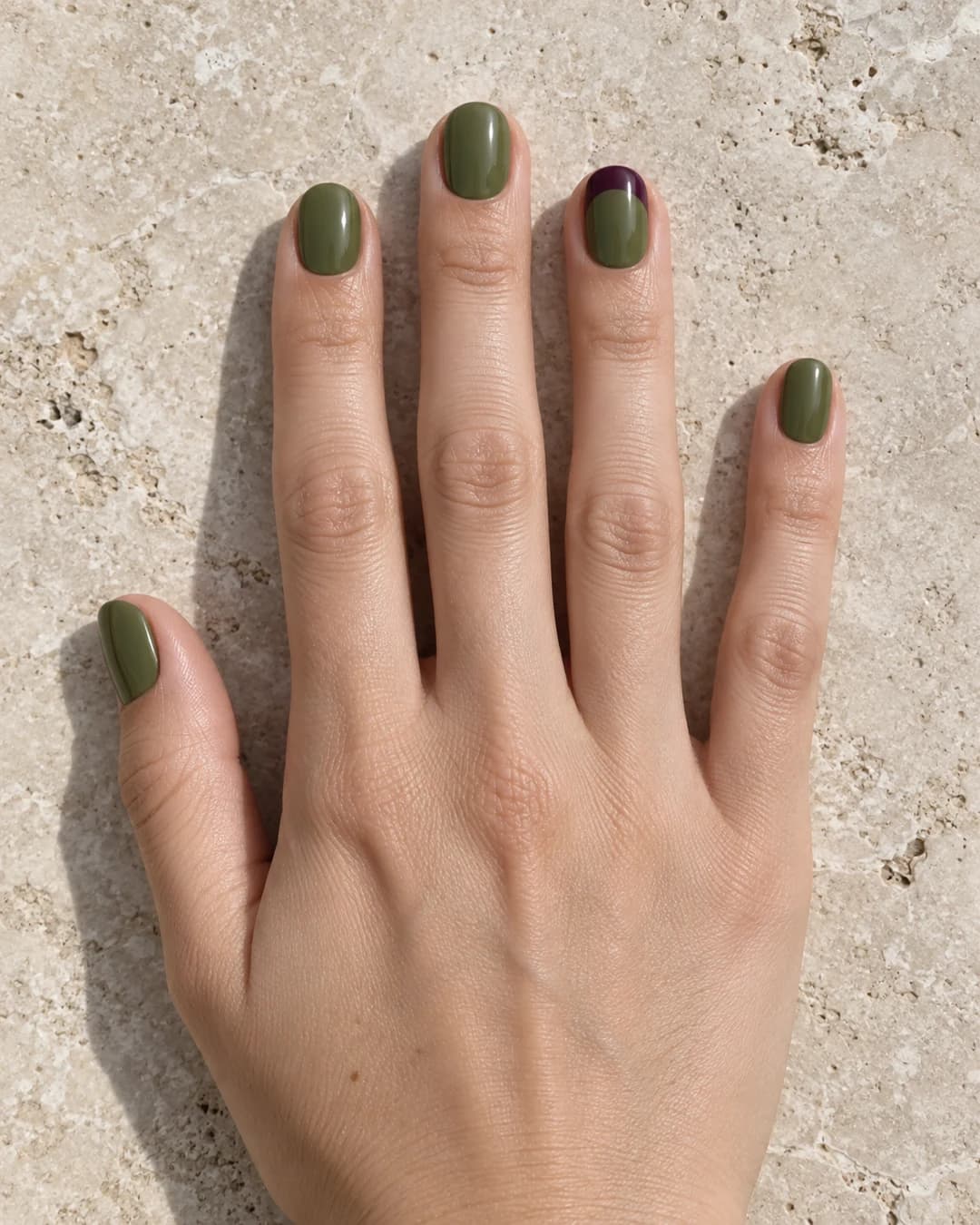 Uñas ovaladas cortas en verde oliva con una punta ciruela sobre piel clara.