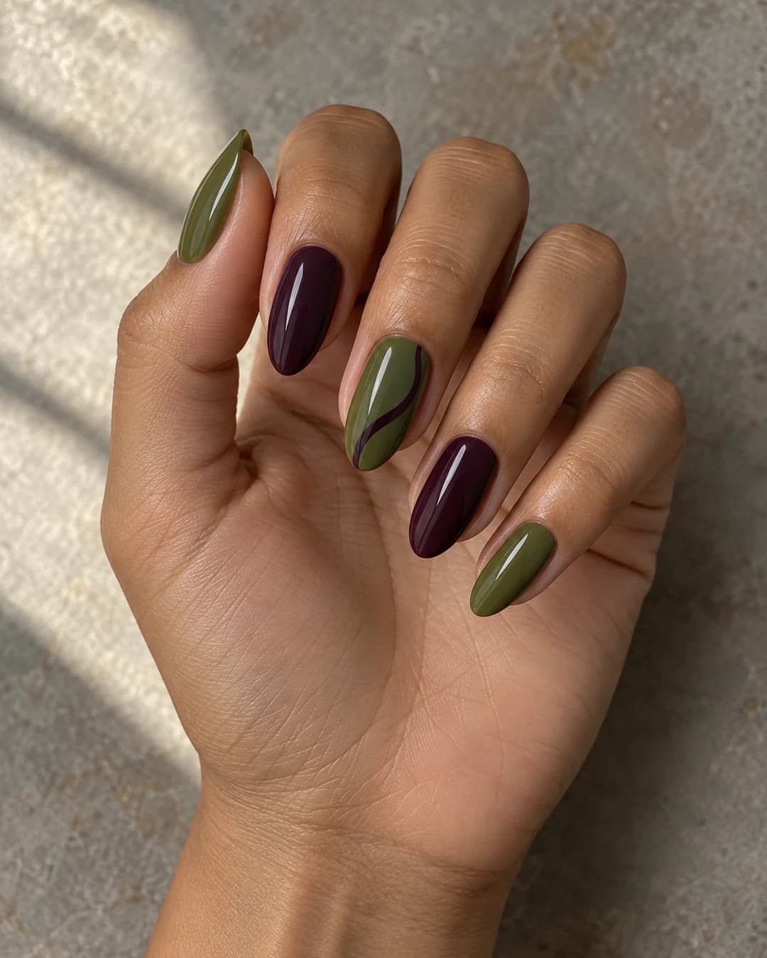 Uñas almendradas medias en verde oliva y ciruela con una curva de acento sobre piel oliva.