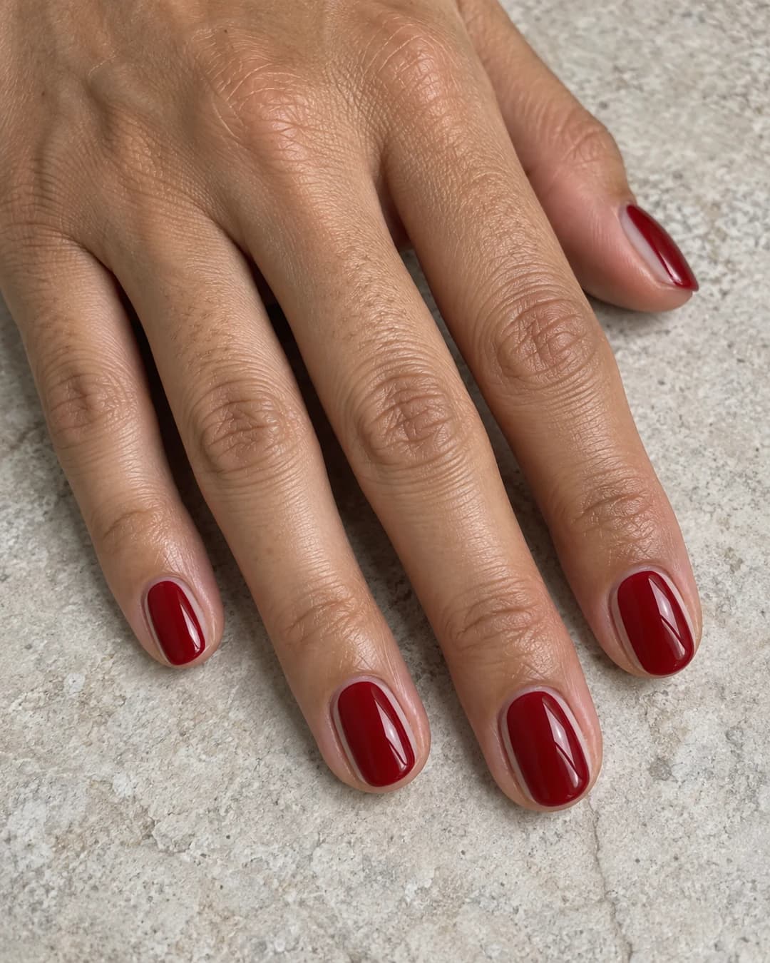 Mano adulta de piel oliva clara con cinco uñas ovaladas cortas en rojo cereza y márgenes naturales finos a ambos lados.