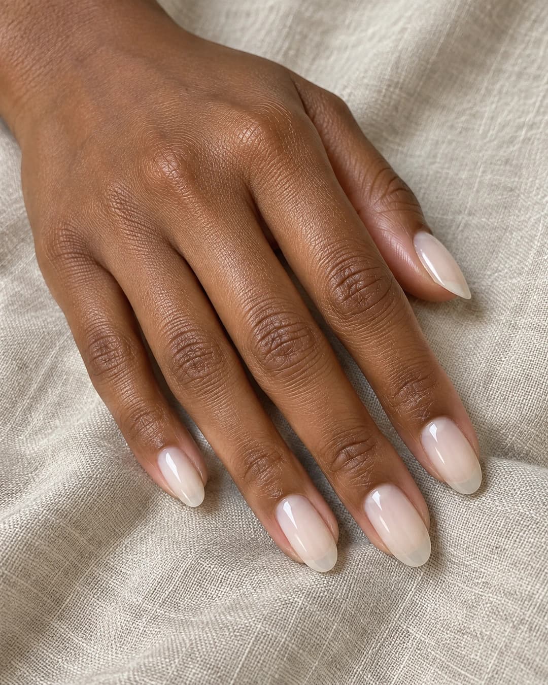 Mano de piel marrón profunda con uñas almendradas medias en blanco vainilla cremoso, translúcido y brillante.