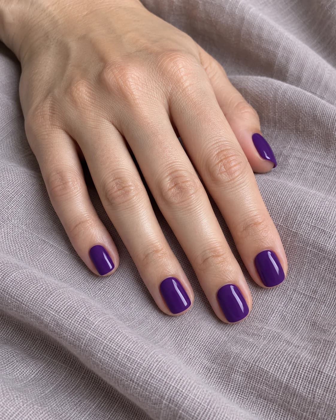 Mano adulta de piel clara con cinco uñas squoval cortas en laca violeta real, opaca y brillante.