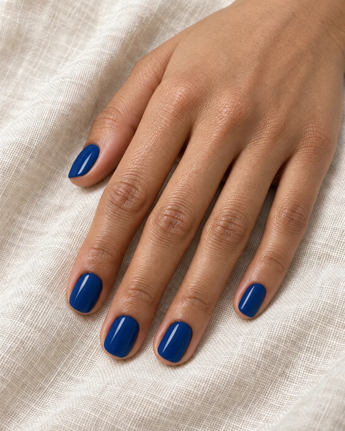 Mano de piel clara con cinco uñas squoval cortas pintadas en azul zafiro brillante.