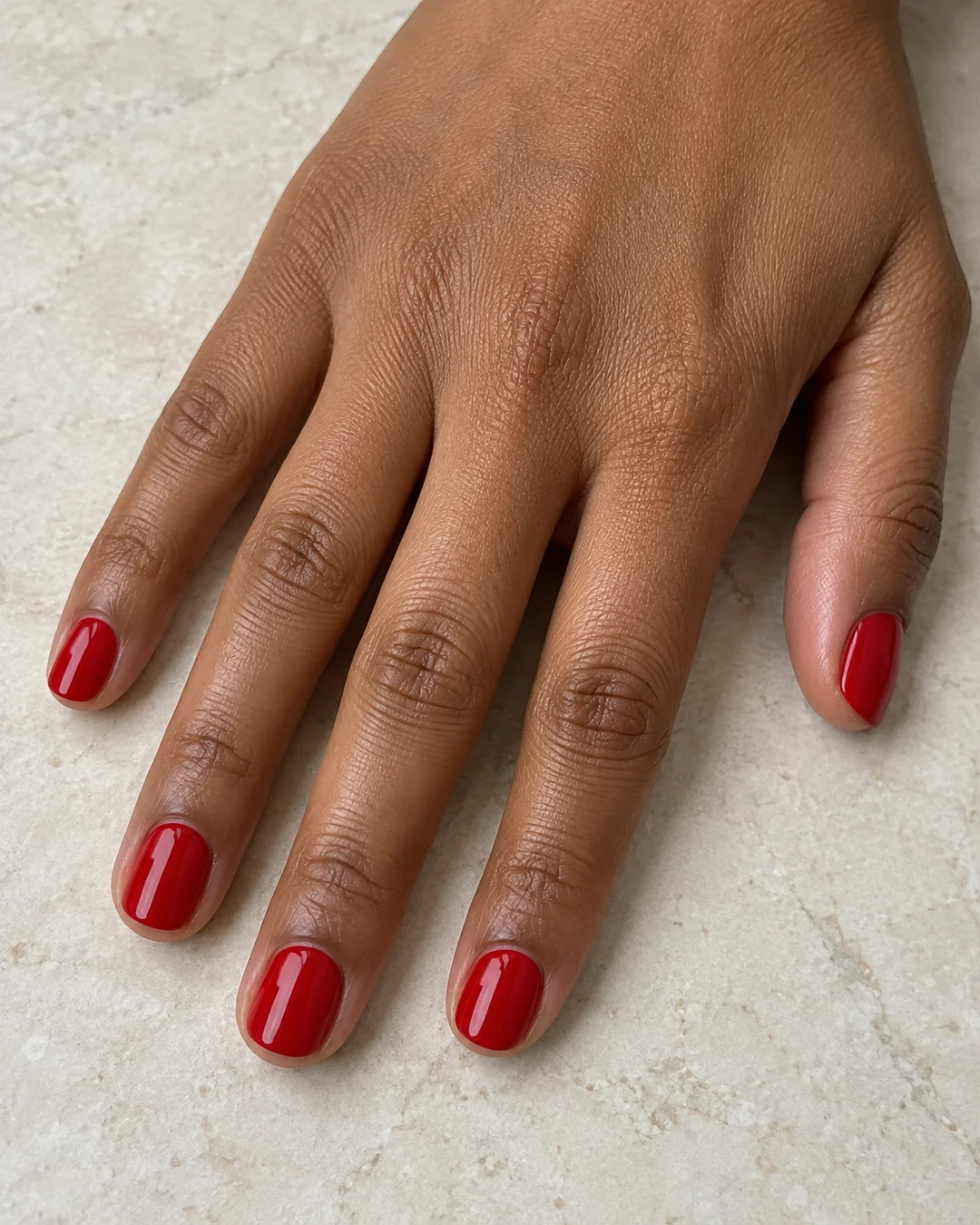 Mano de piel marrón media con uñas cortas redondeadas en rojo cereza brillante.