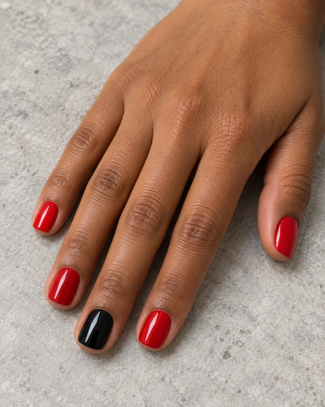 Uñas cortas de esquinas suaves en rojo brillante y una uña negra de acento. Detalle de las uñas.