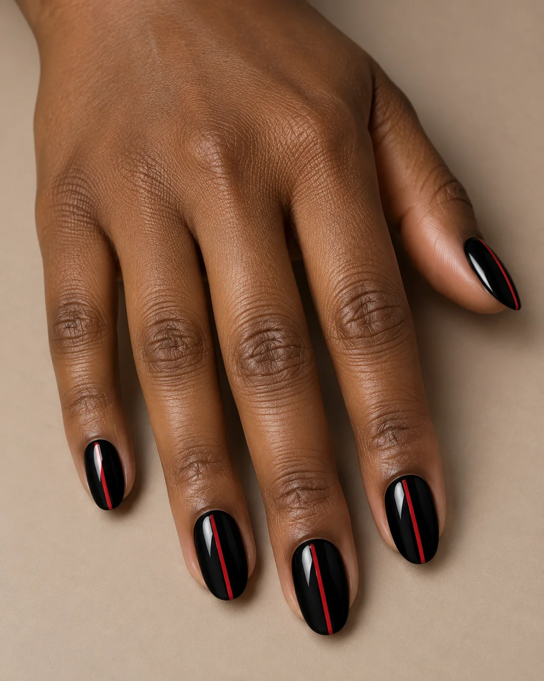 Uñas ovaladas medias negras y brillantes con una línea roja fina longitudinal. Detalle de las uñas.