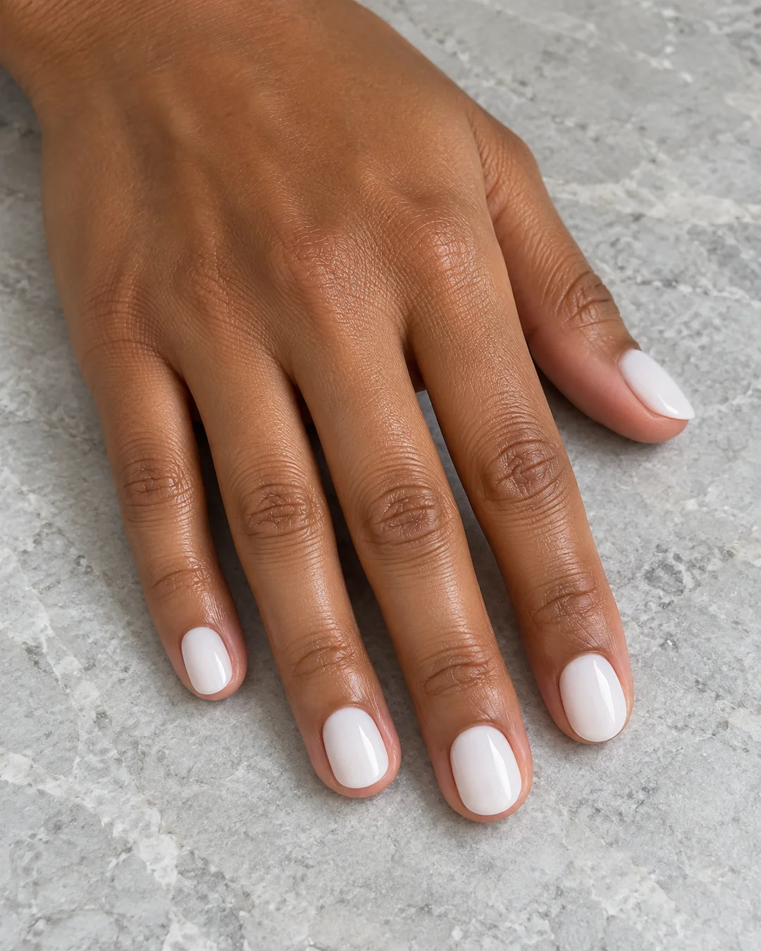 Uñas cortas redondeadas en blanco lechoso brillante y sin decoración. Detalle de las uñas.