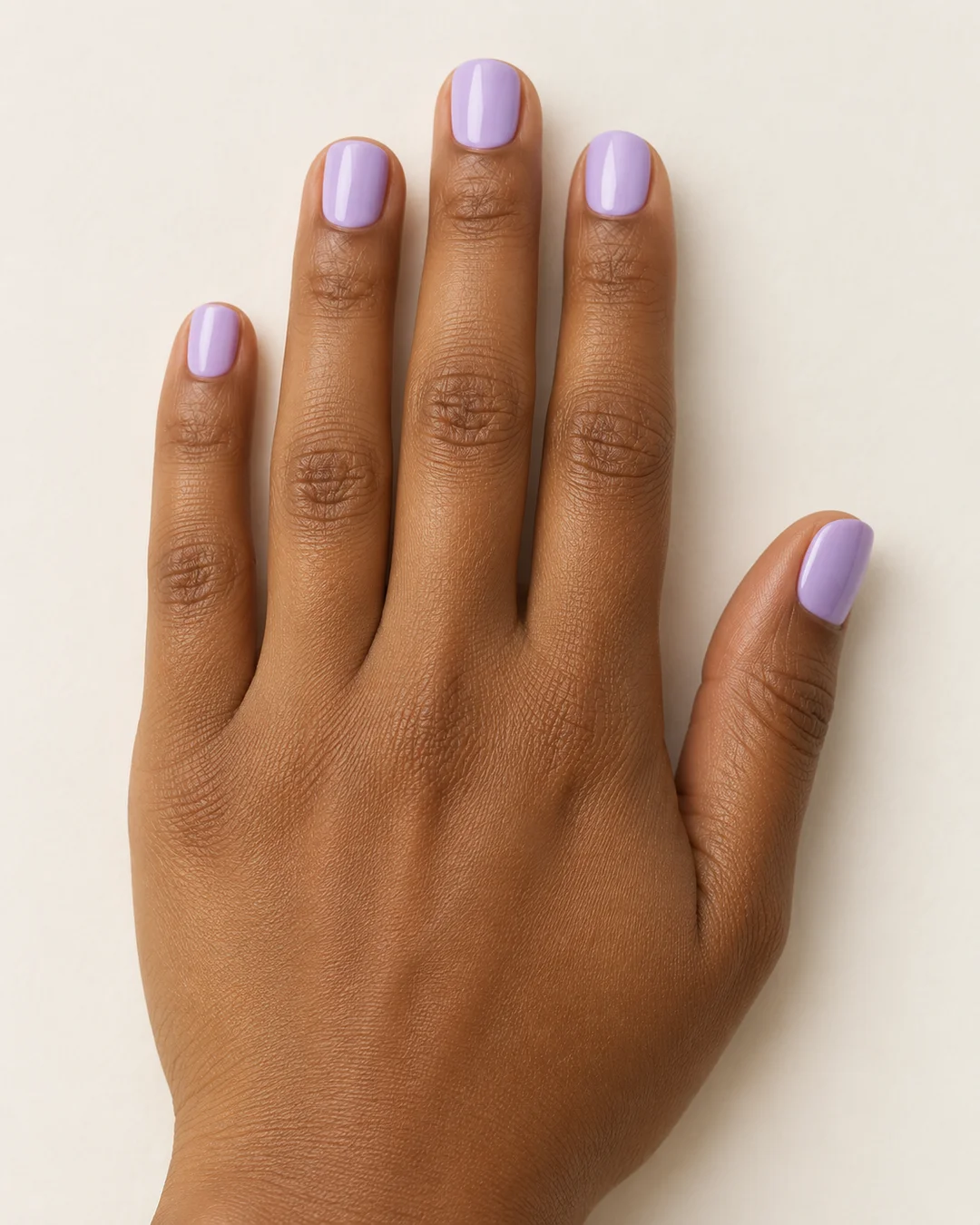 Uñas cortas cuadradas de esquinas suaves en lila pastel uniforme y brillante. Detalle de las uñas.